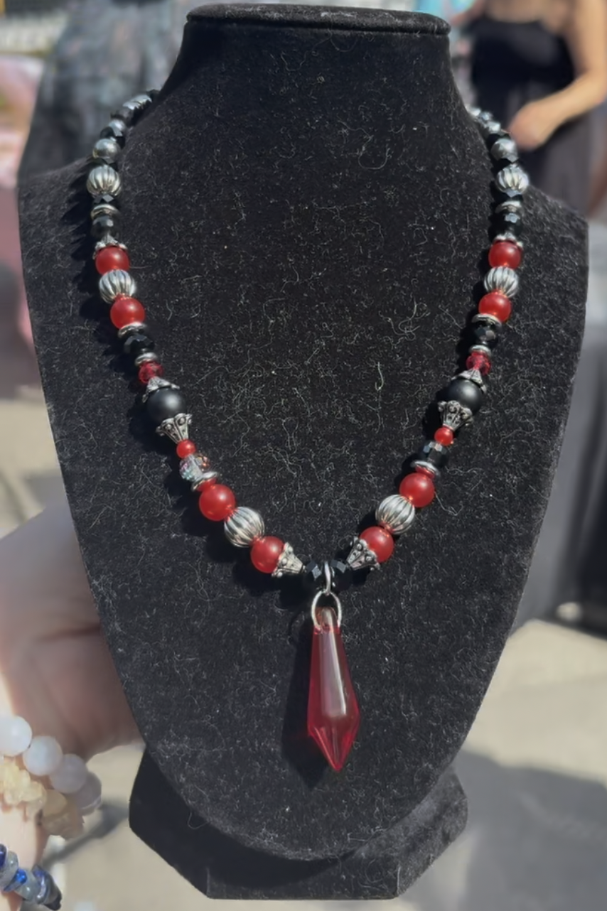 Necklace displayed on black velvet bust, featuring red, black, and silver beads with a large red pendant.