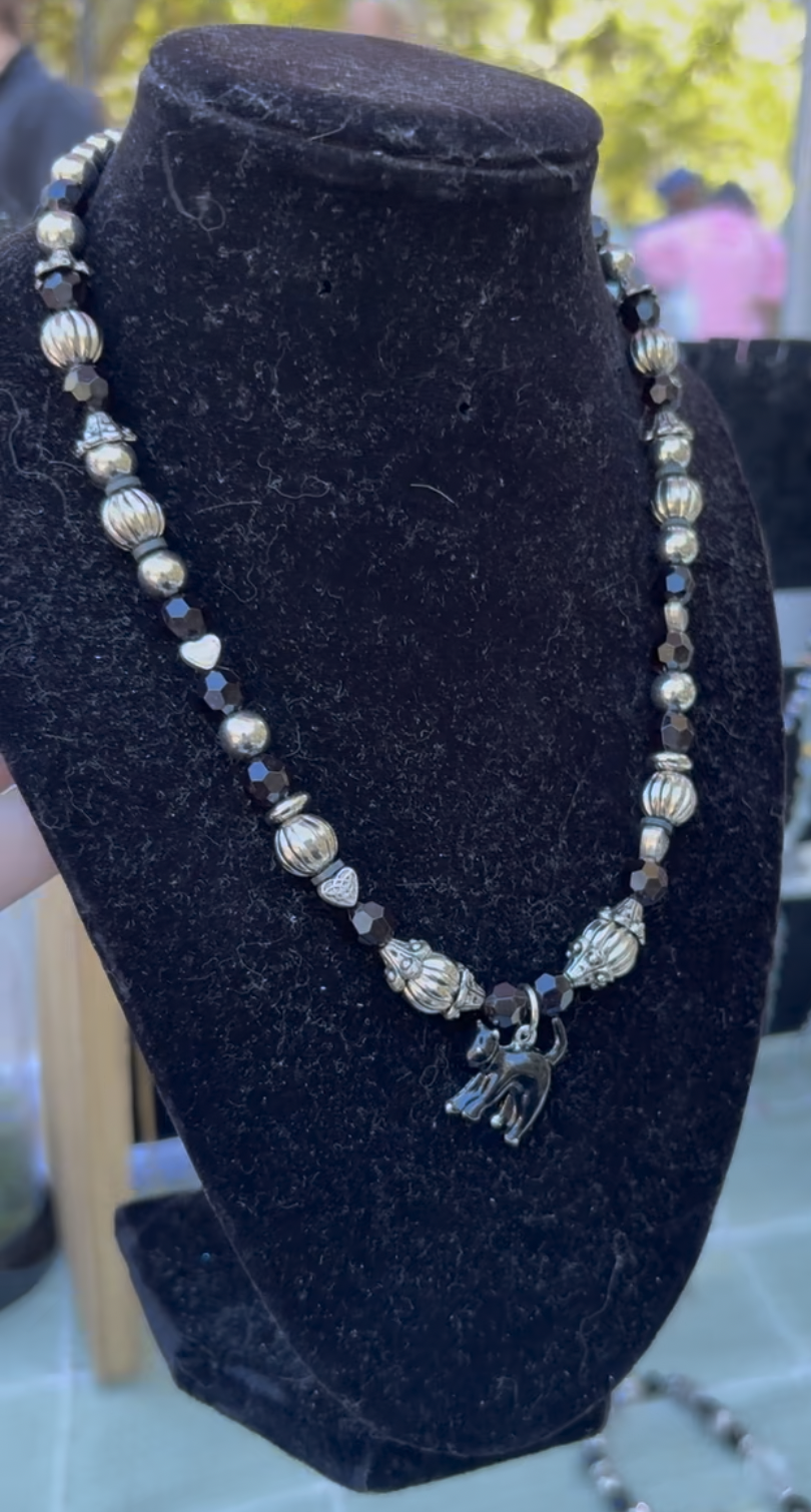 Silver and black beaded necklace with a cat charm on a black display stand.