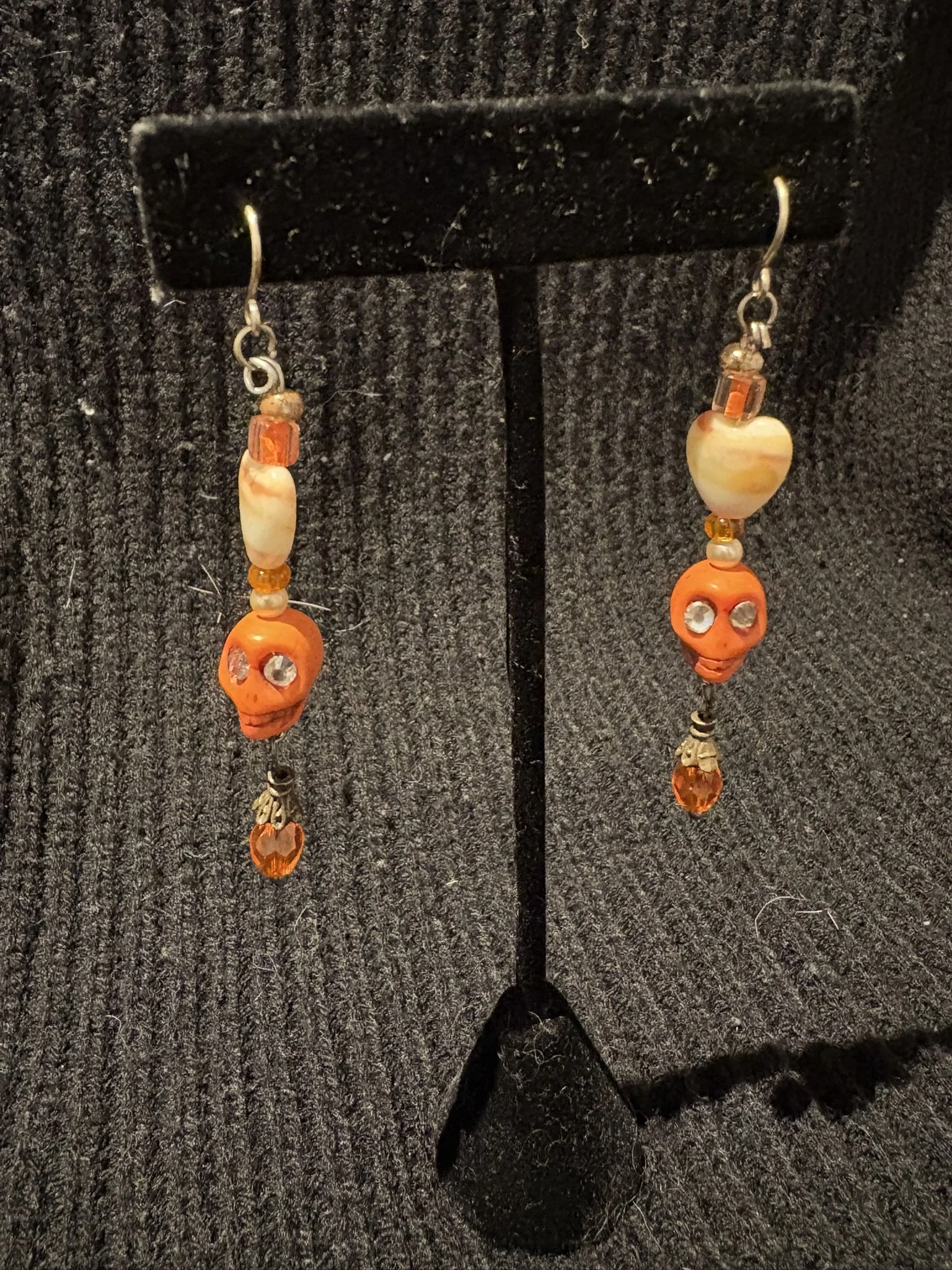 Pair of Halloween-themed earrings with orange skull and beads, hanging on a black display stand.