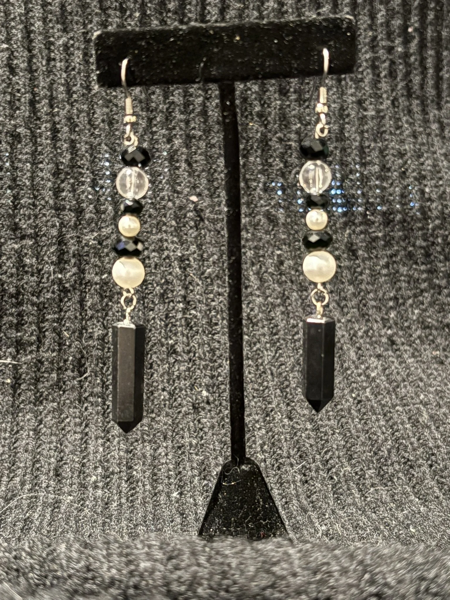 Black and silver beaded earrings hanging on a black display with a textured gray background.