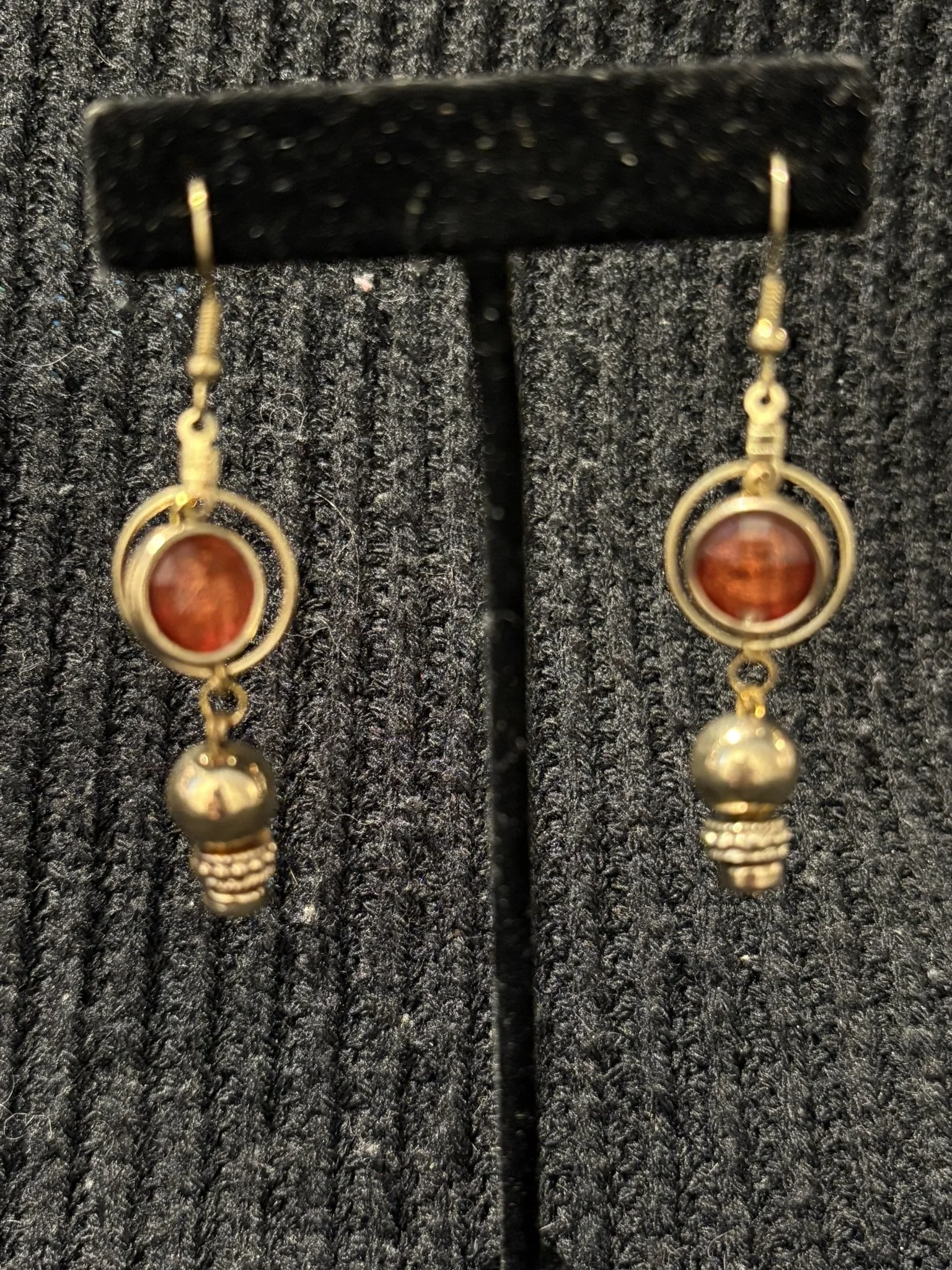 Pair of gold and orange dangling earrings displayed on a black textured surface.