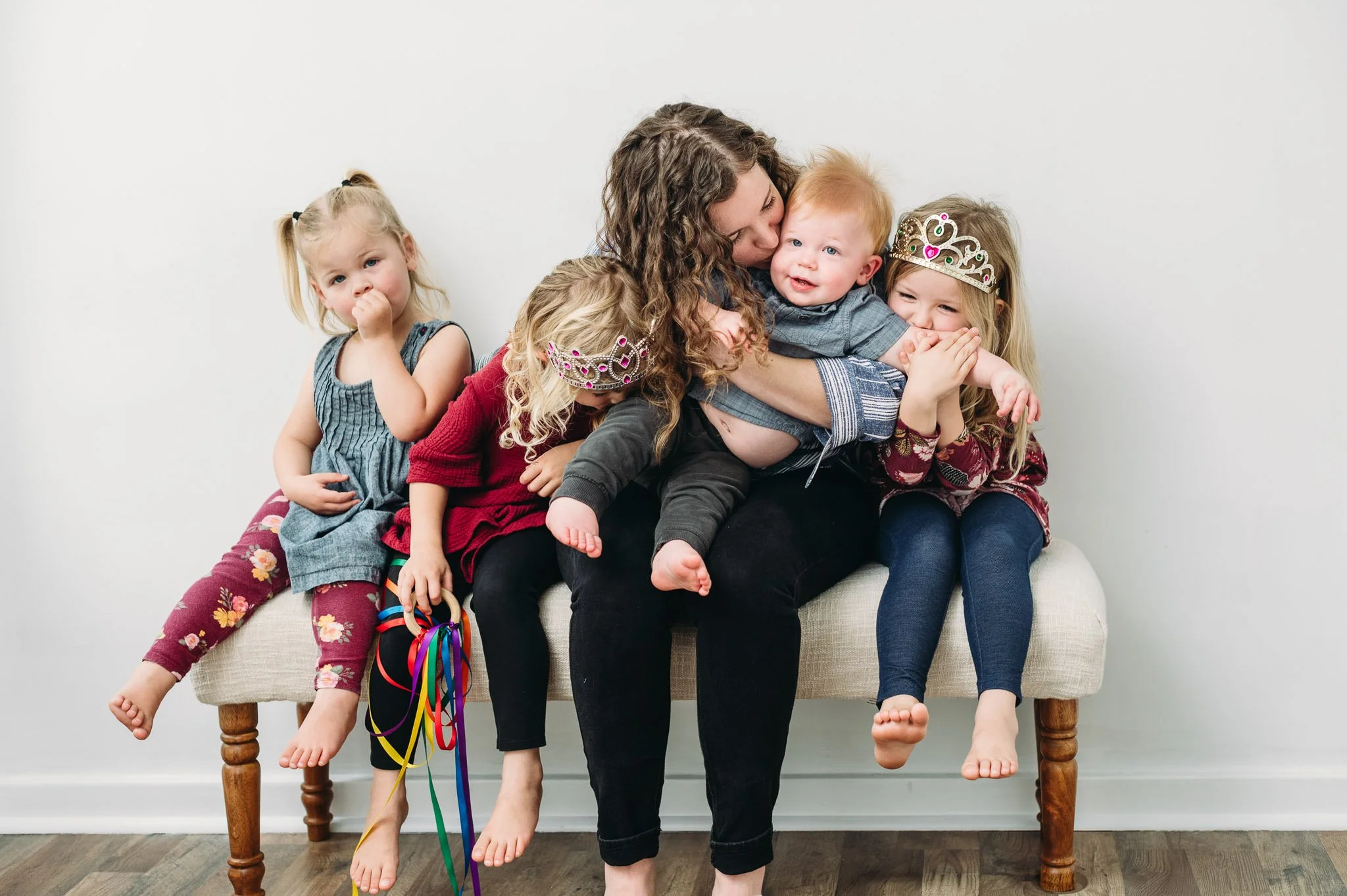 Motherhood photography in Bend, Oregon of mother and children piled onto a bench wearing crowns and holding ribbon wands.