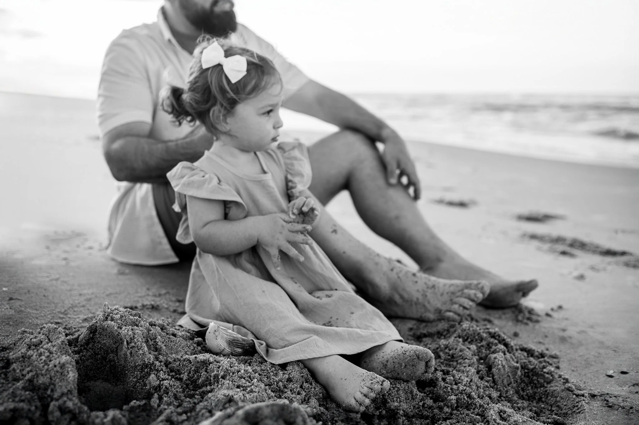 Toddler girl sitting in the sand with her father during a lifestyle family photoshoot, by Elise Souders, photographer