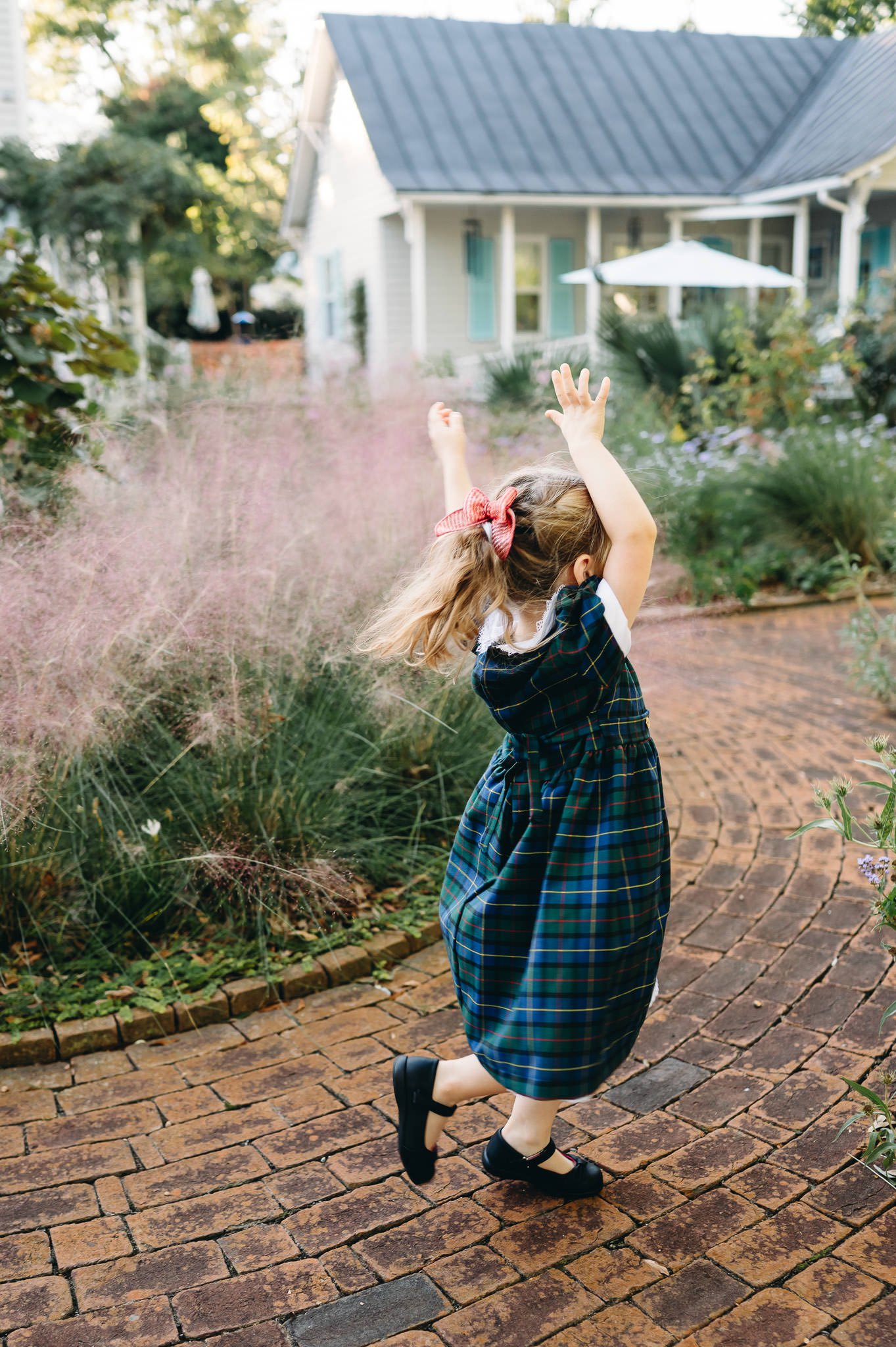 A young girl twirls on a brick path in a neighborhood garden wearing a plaid dress lifestyle family session in Bend, Oregon.