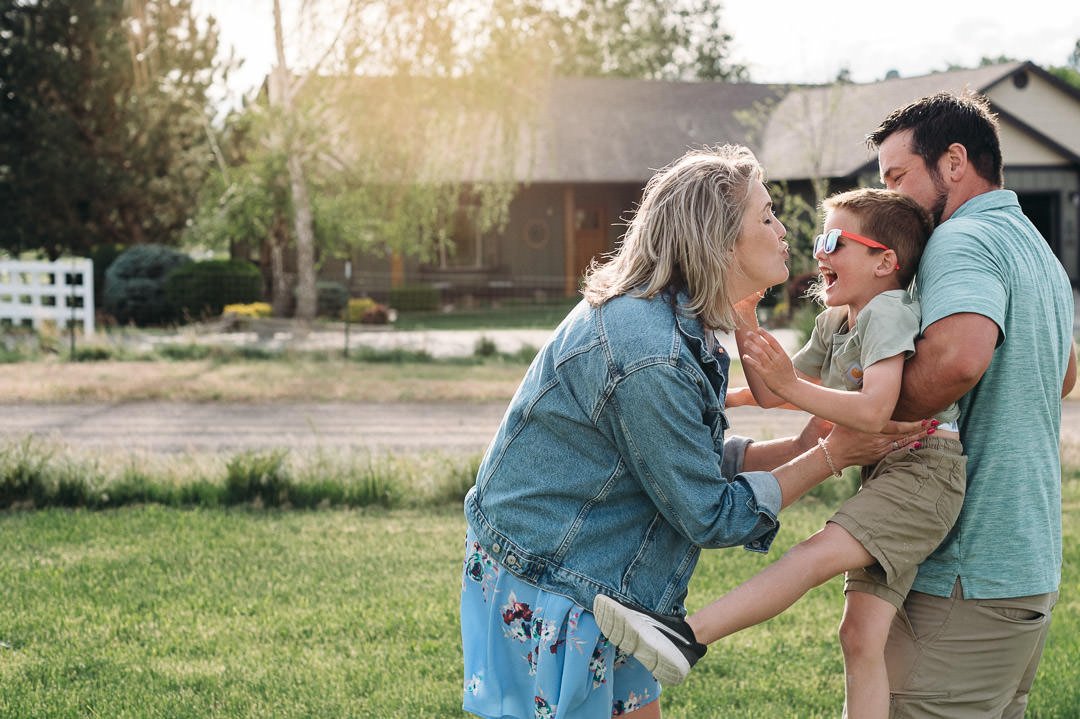 Parents playfully hugging and kissing son in backyard documentary session, by Elise Souders Bend, Oregon photographer