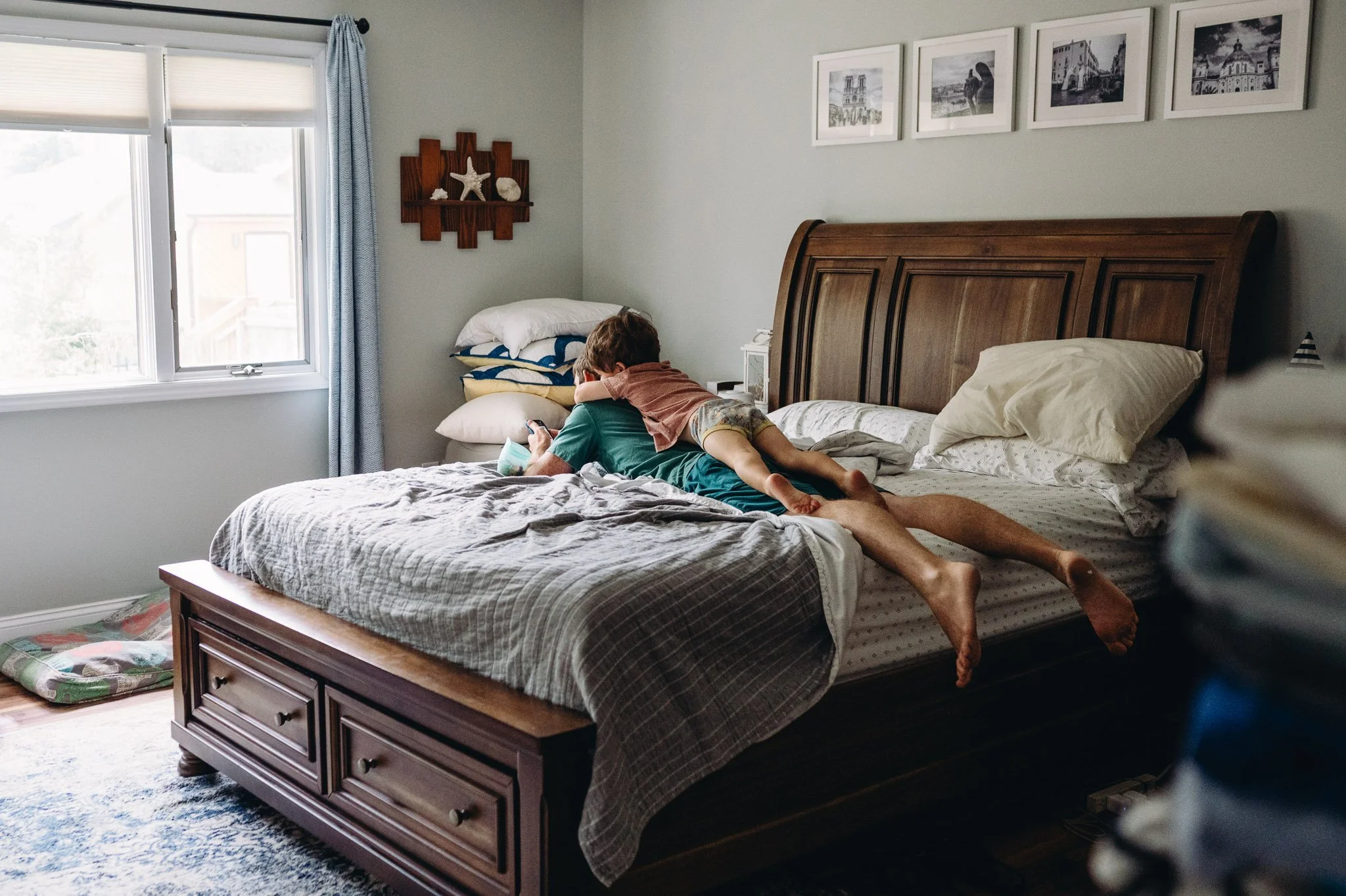 a son lays on top of his father in a messy bedroom in an intimate moment, documentary photograph 