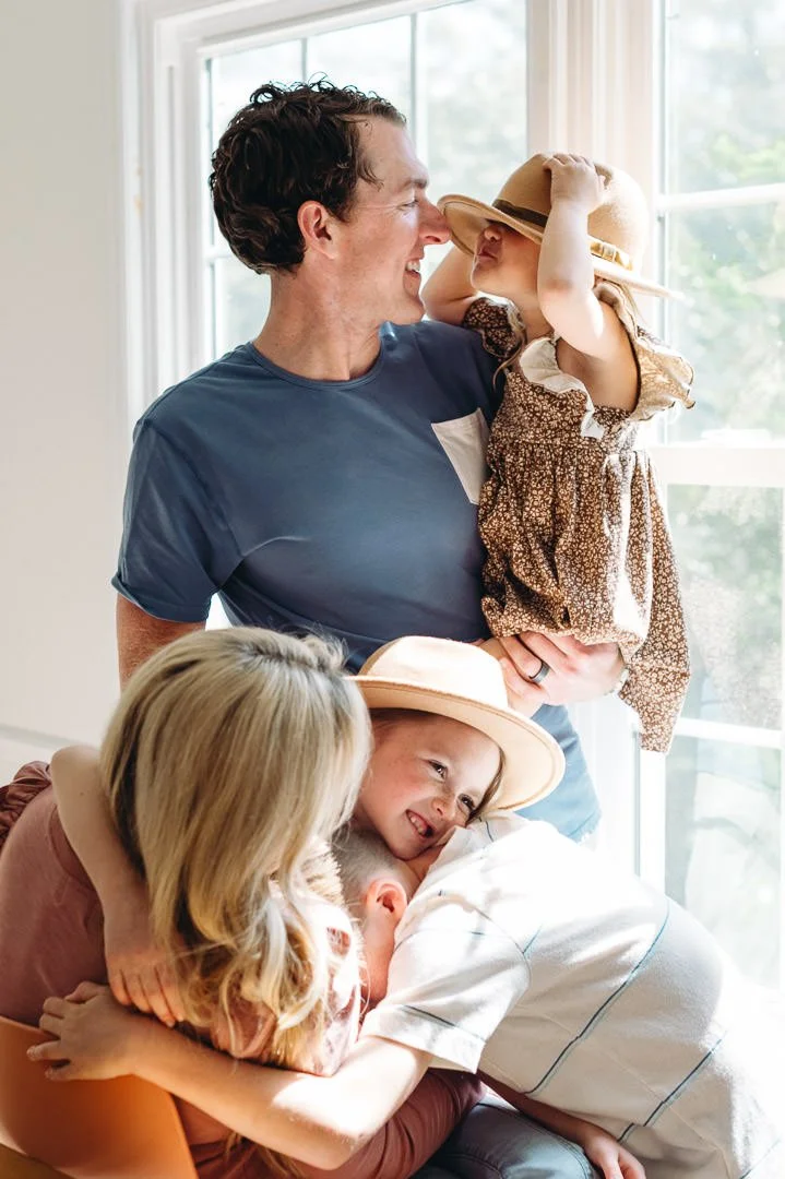 Family snuggled near large window for their family photos at home.
