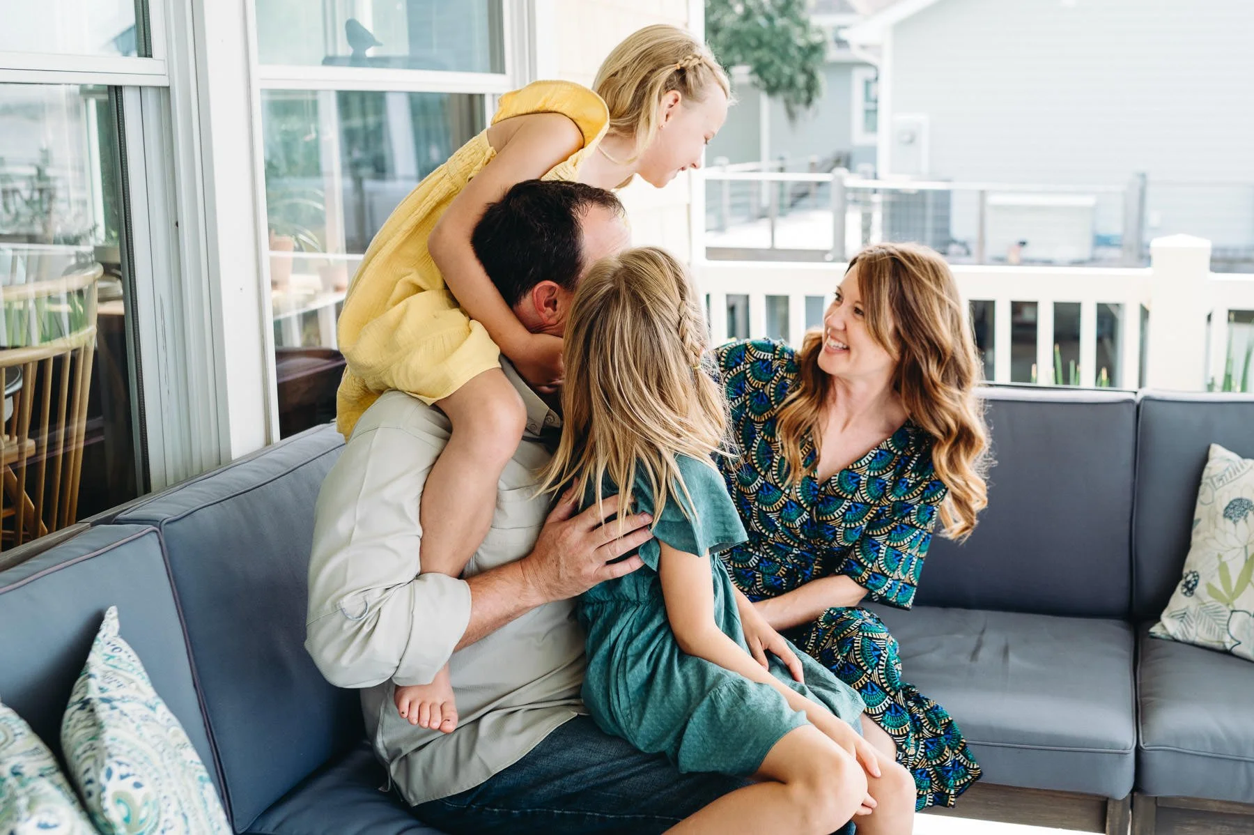 Girls sitting on father's lap and shoulders laughing with mother, genuine family moment by Elise Souders, Bend Family Photography