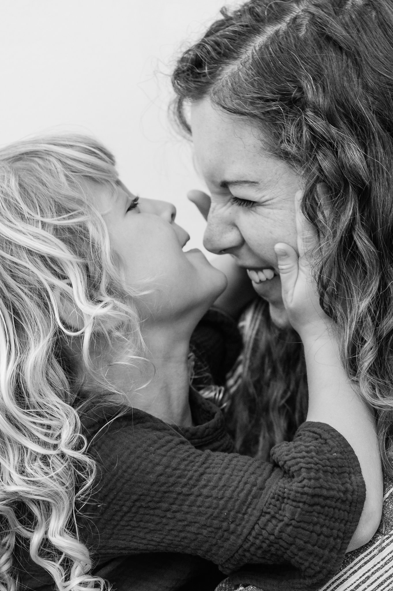 A woman and a young girl are about to kiss, their noses touching and eyes closed, showing affection and closeness.