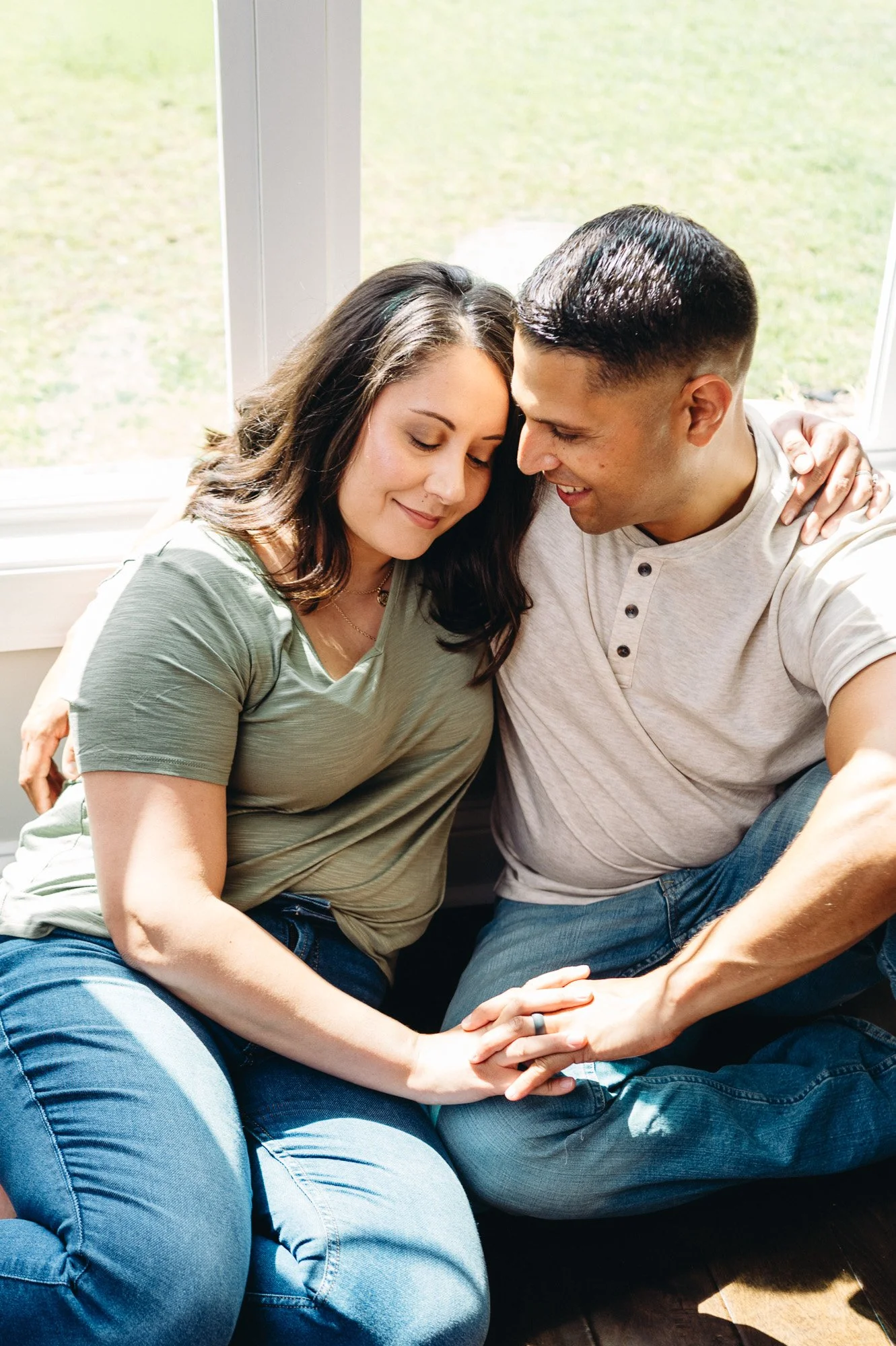 Affectionate couple sitting together by a sunny window, holding hands and smiling