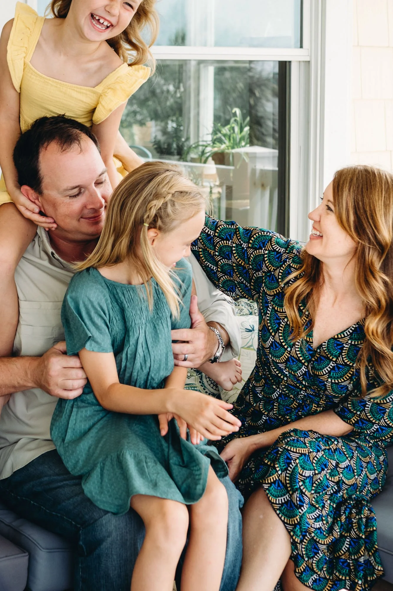 Family with two daughters piled on top of dad, mother laughing while she reaches for children. Photo by Elise Souders, Bend Oregon Photographer.