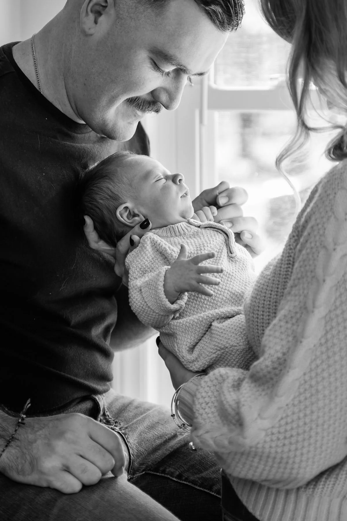 Parents with new baby by bright window light, emotive black and white image by Elise Souders, Bend Family Photographer
