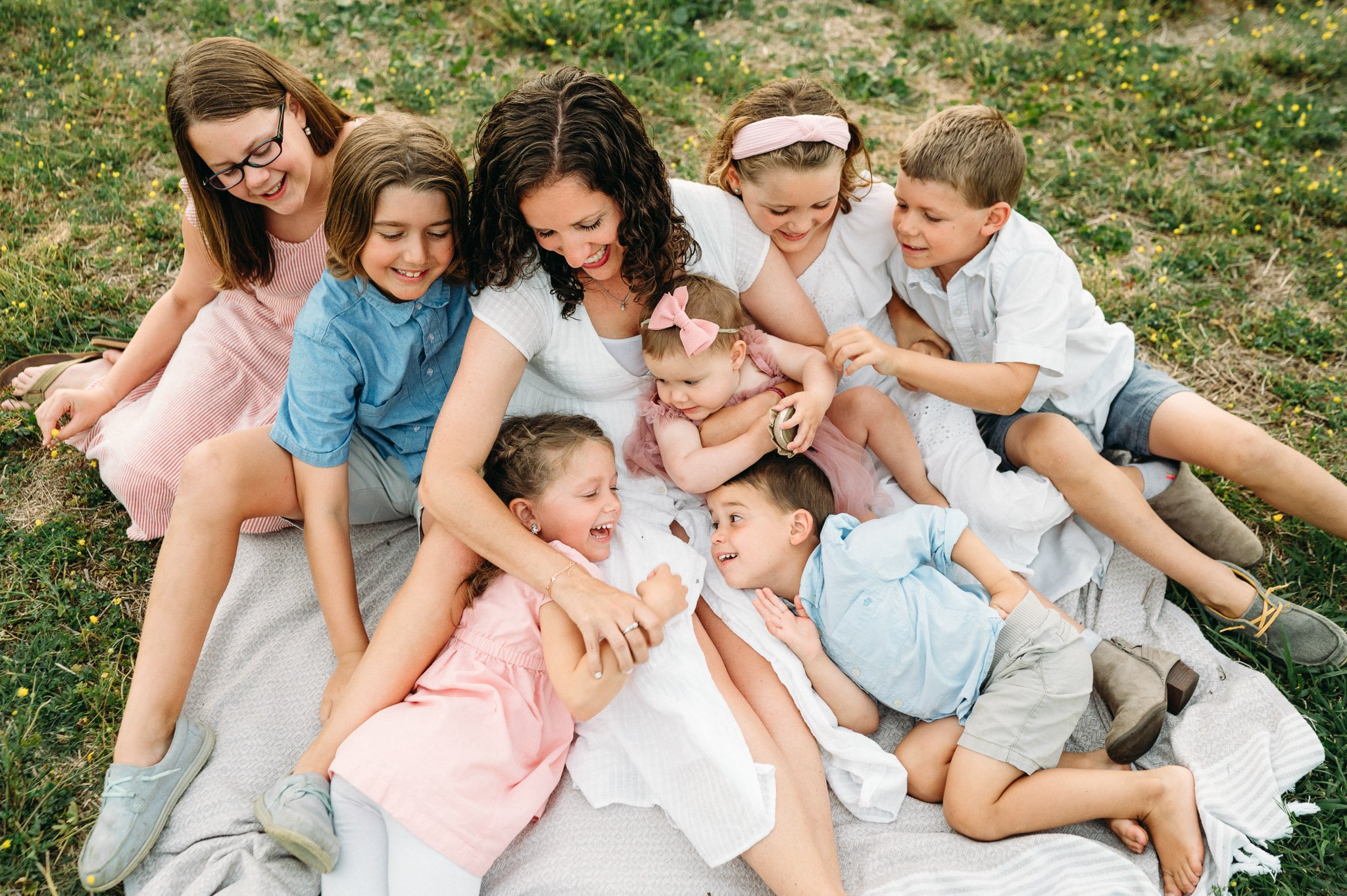 Motherhood photoshoot in Central Oregon with kids piled on top of mom, everyone is wearing white, blue, or pink clothing.