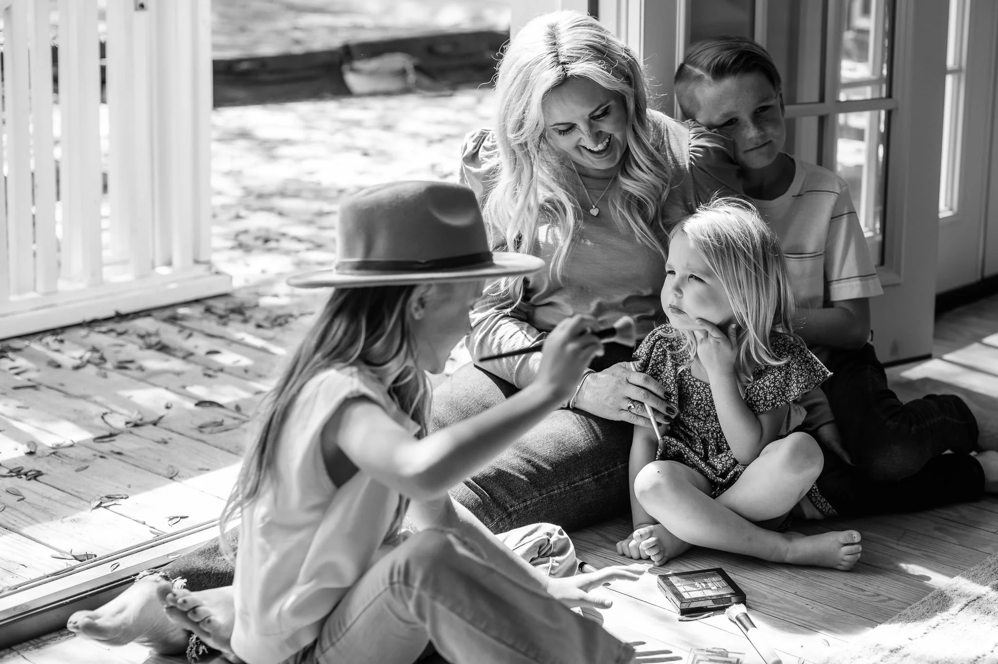 A family sitting on a wooden porch with large windows, enjoying a sunny day black and white documentary family photography by Elise Souders