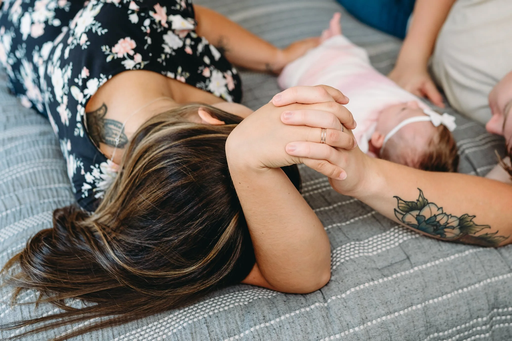 Detail of husband and wife with entwined hands, laying on their bed with their baby girl, in-home newborn photo Bend, Oregon by Elise Souders, photographer