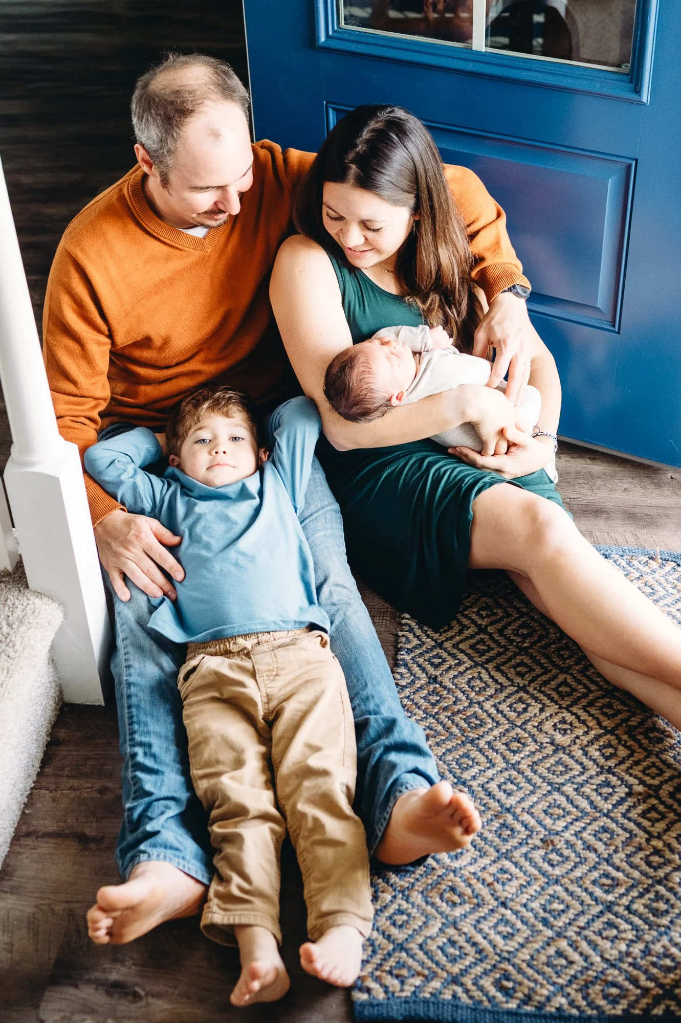 Parents with toddler and newborn baby cuddled up by a bright blue door, newborn photo by Elise Souders, Bend Oregon Photographer