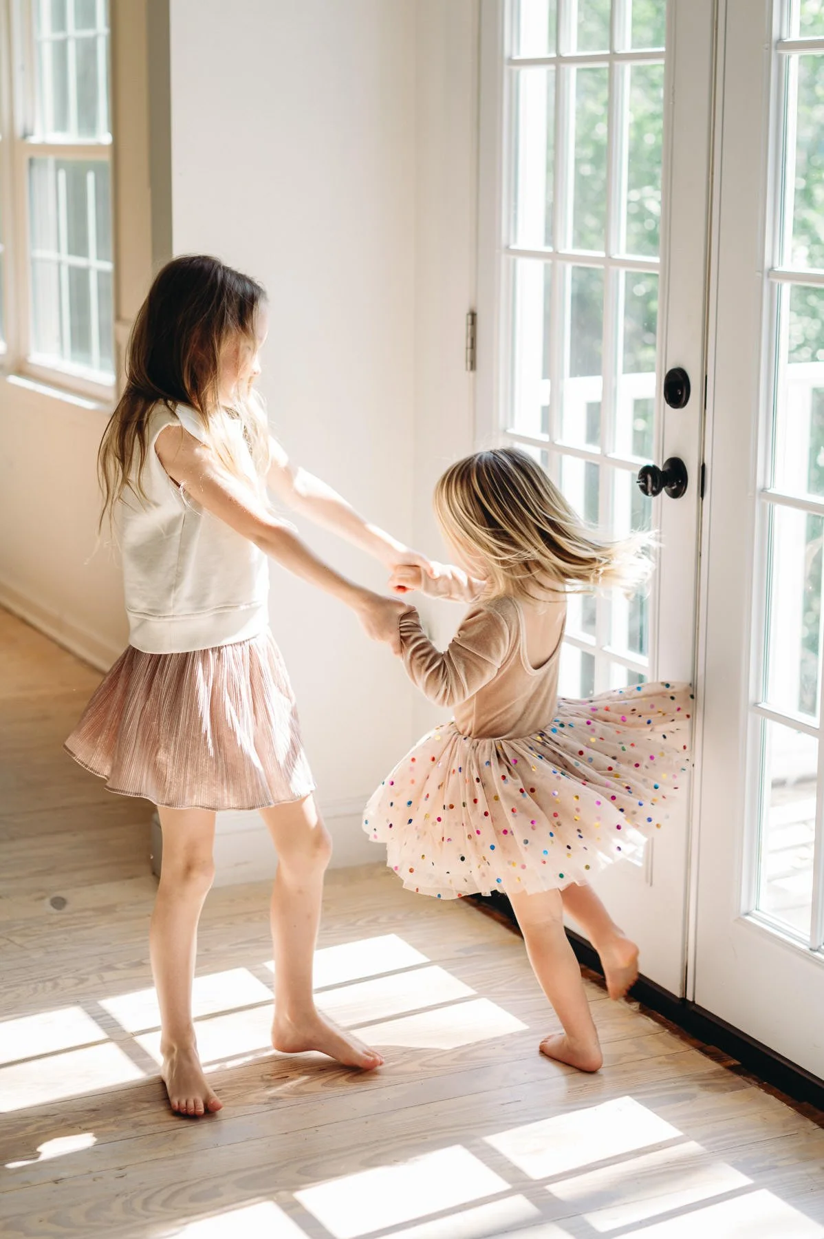 Unposed image of sisters dancing in tutus near bright window, by Elise Souders, Bend Family Photography
