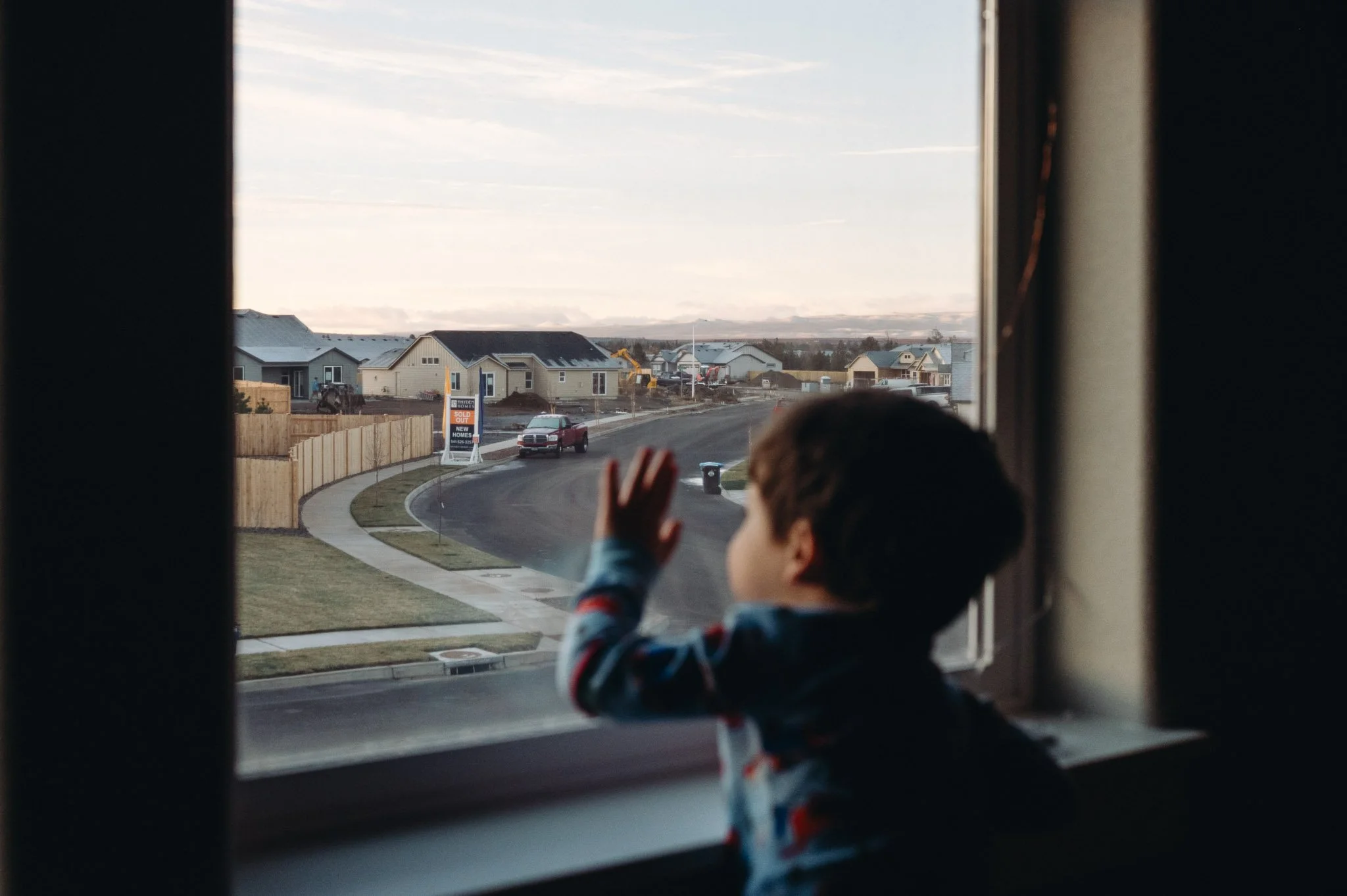 a young boy looks out the window at construction equipment in a neighborhood, Bend documentary photographer