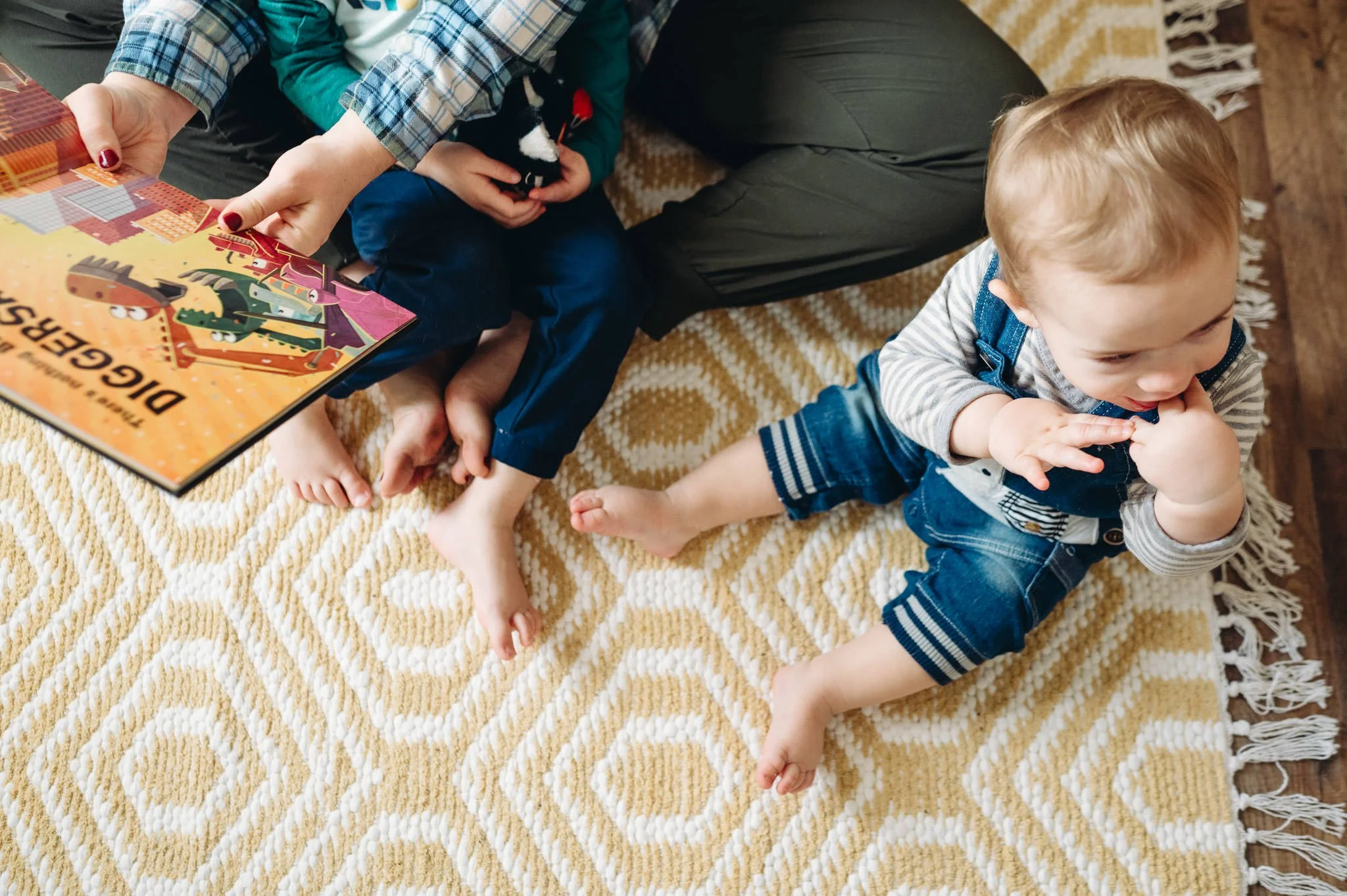 lifestyle motherhood photography in Bend overhead shot of a mother and two boys reading, showing their legs entwined and the books and toys on a carpet.