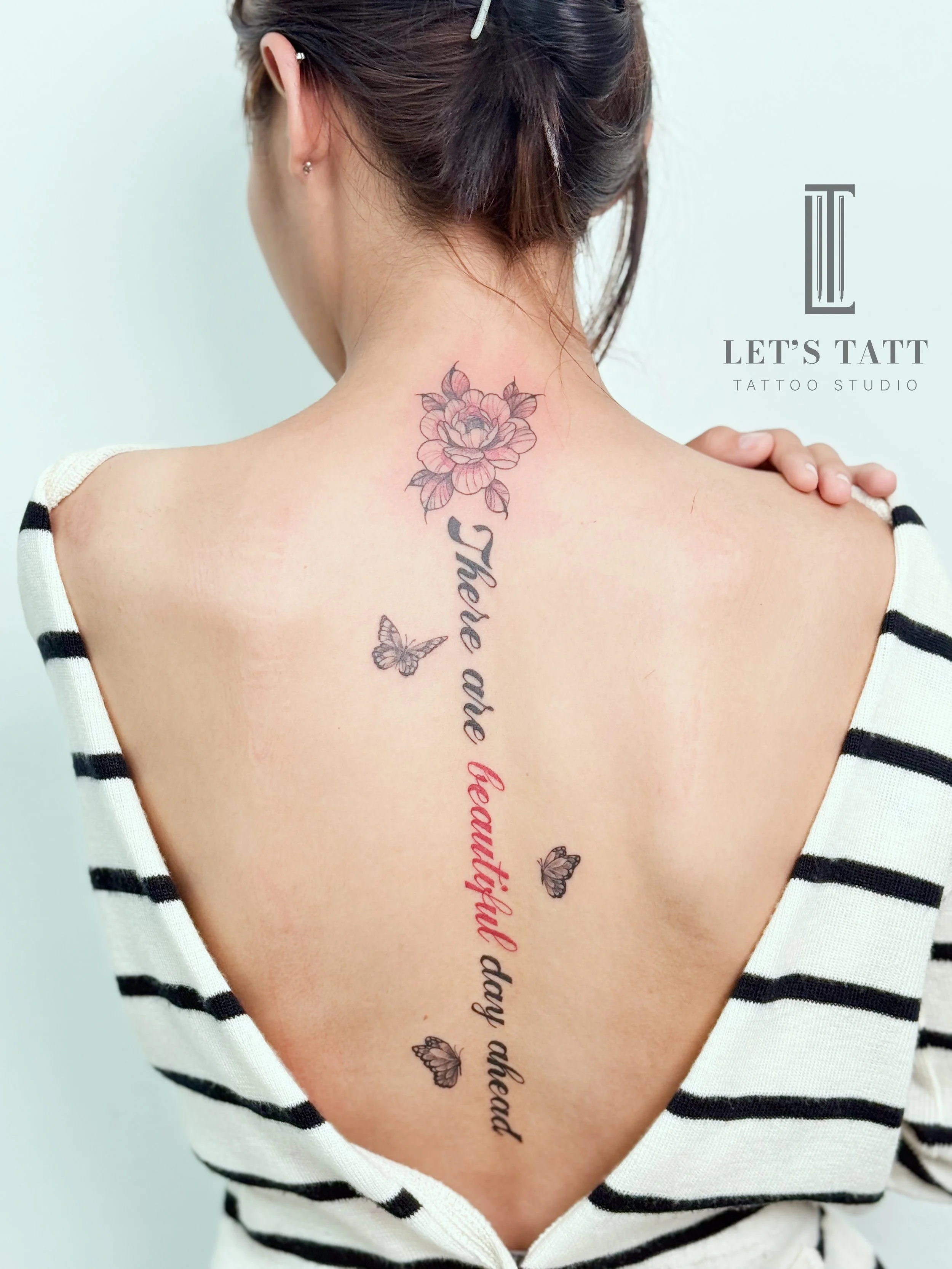 รอยสักดอกไม้และตัวอักษรสไตล์ Fine Line บริเวณแผ่นหลังจาก Let’s Tatt Studio / Fine line floral and lettering tattoo by Let’s Tatt Studio Chiang Mai ดอกไม้และลายเส้นที่เรียงตัวตามแนวกระดูกสันหลัง สื่อถึงการเติบโต ความอ่อนโยน และตัวตนที่ค่อย ๆ เบ่งบานตา