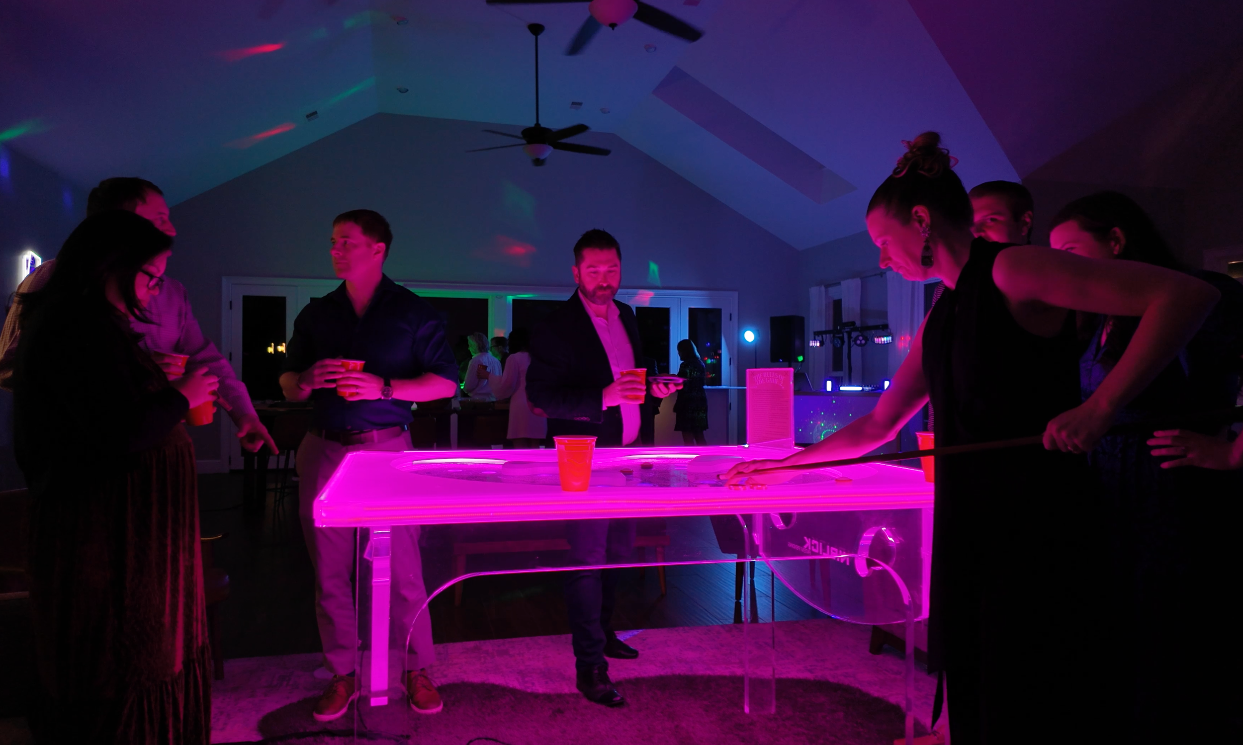Group of people playing air hockey in a dimly lit room with colorful lights.