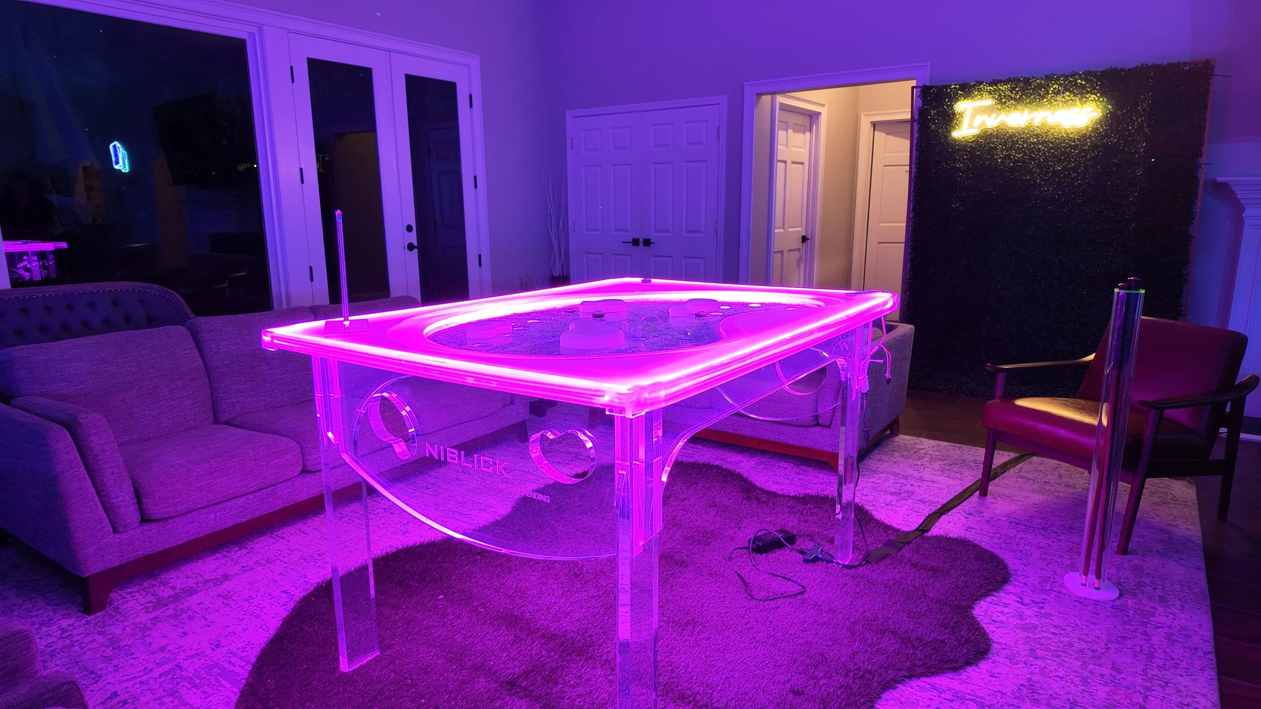 Living room with neon purple ping pong table, gray sofa, purple armchair, and neon sign reading 'Inspire' on a decorative wall.
