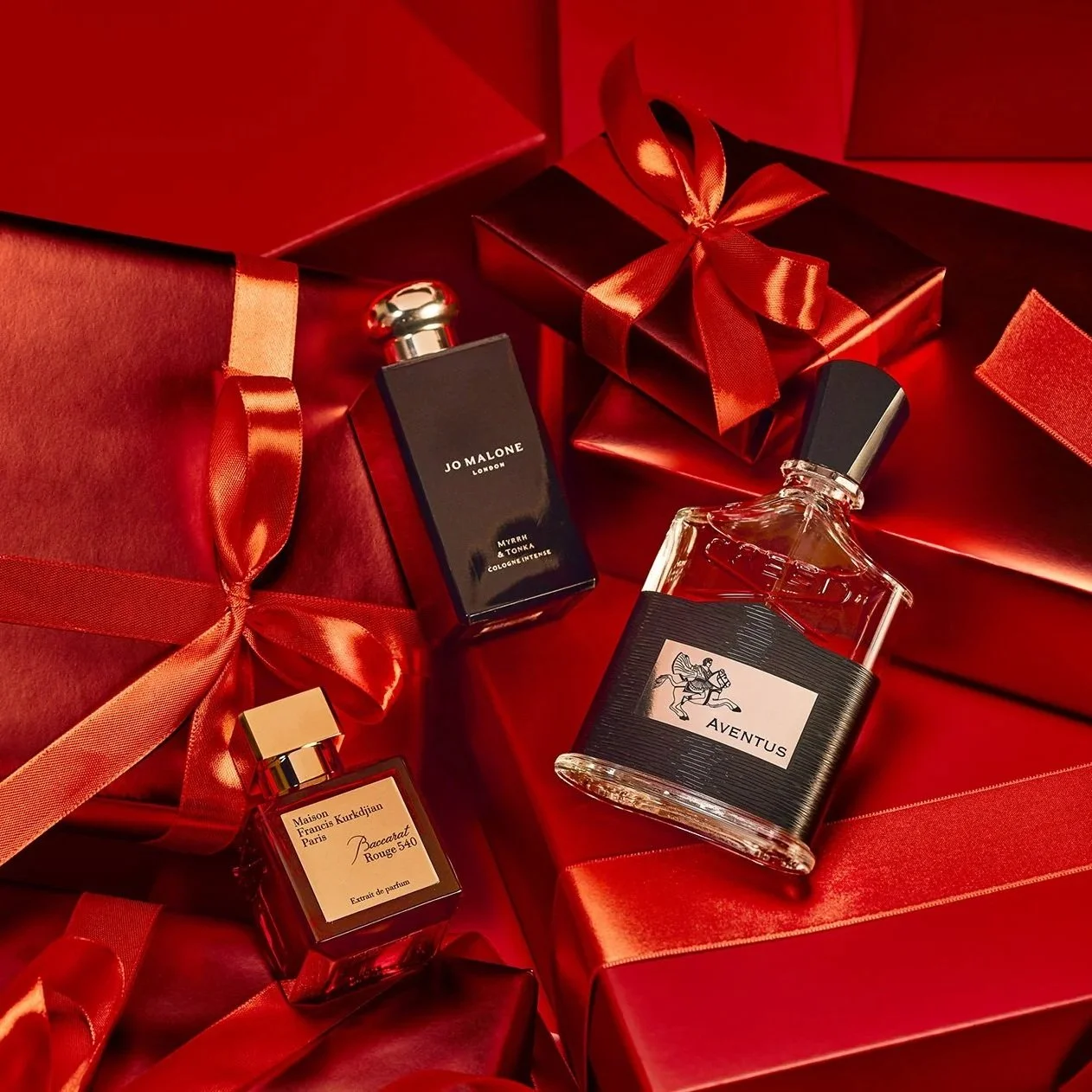 Assorted perfume bottles surrounded by red gift boxes wrapped with red ribbon.