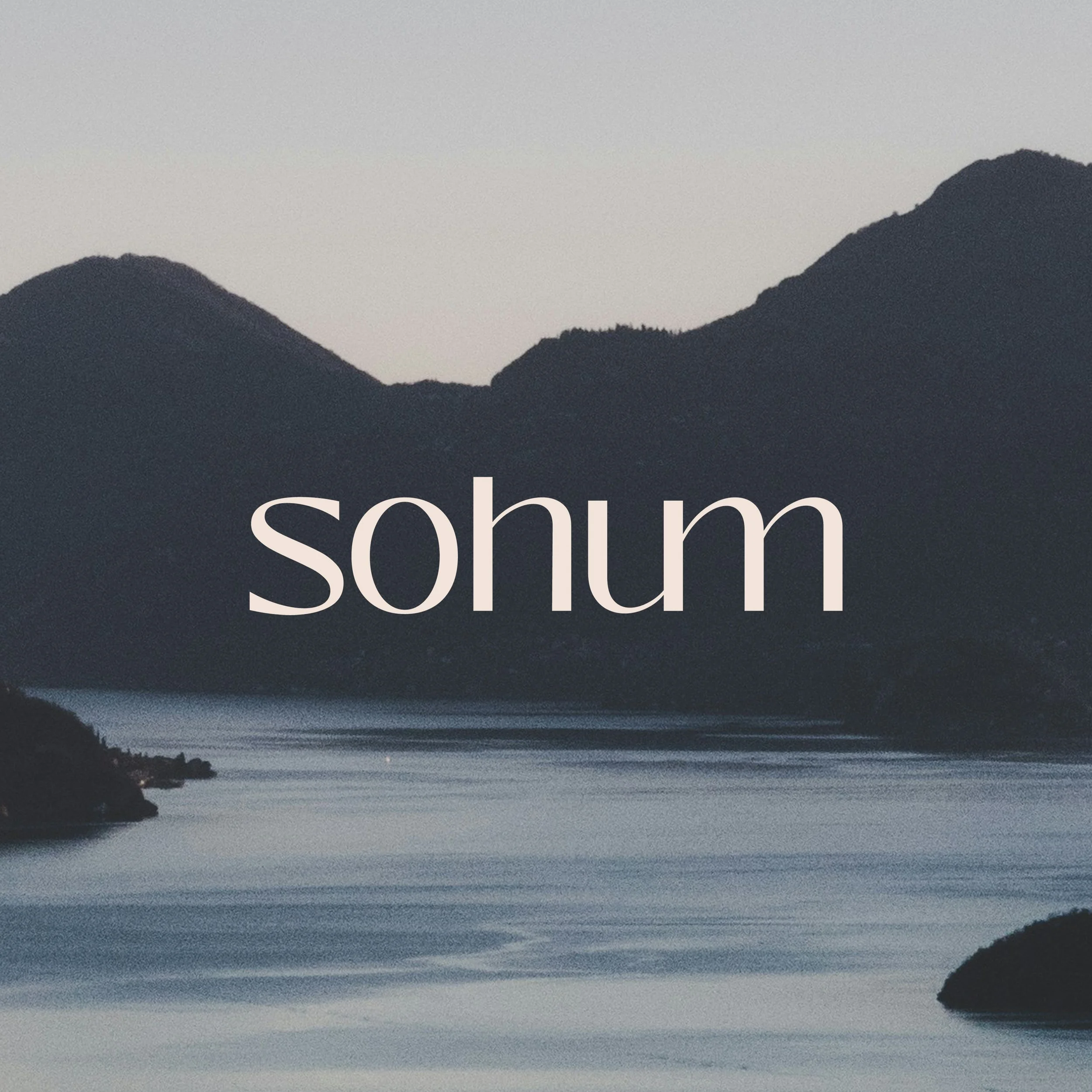 Calm lake surrounded by mountains at dusk with the word 'sohum' overlayed.