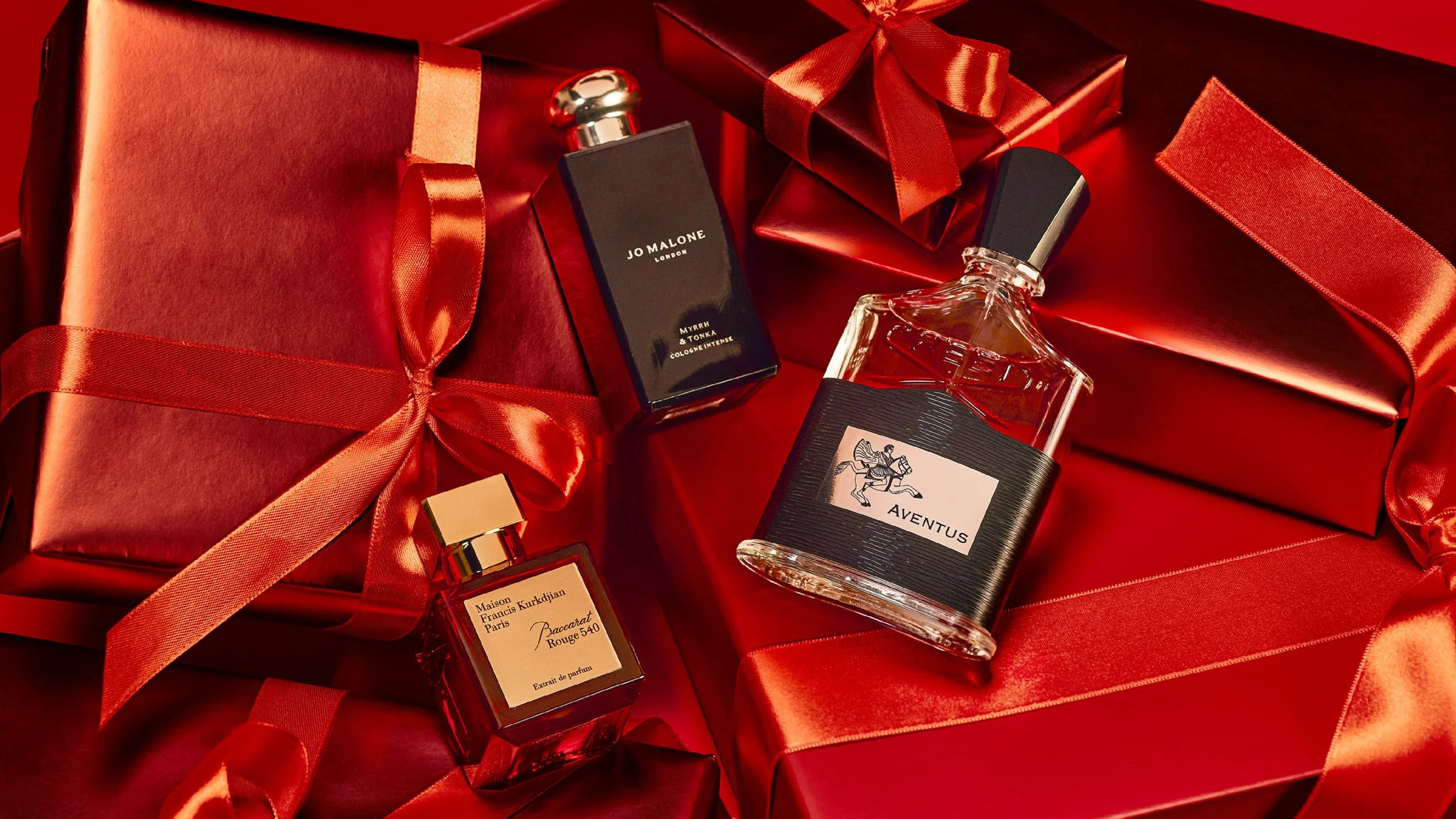 Luxury perfume bottles and red gift boxes wrapped with satin ribbons on a red satin background.