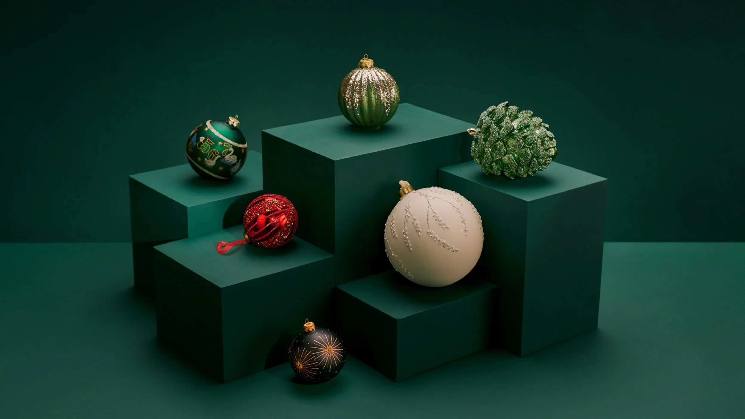 Six Christmas ornaments on green display boxes against a dark green background, including glittery, painted, and decorated baubles in red, green, white, and black.