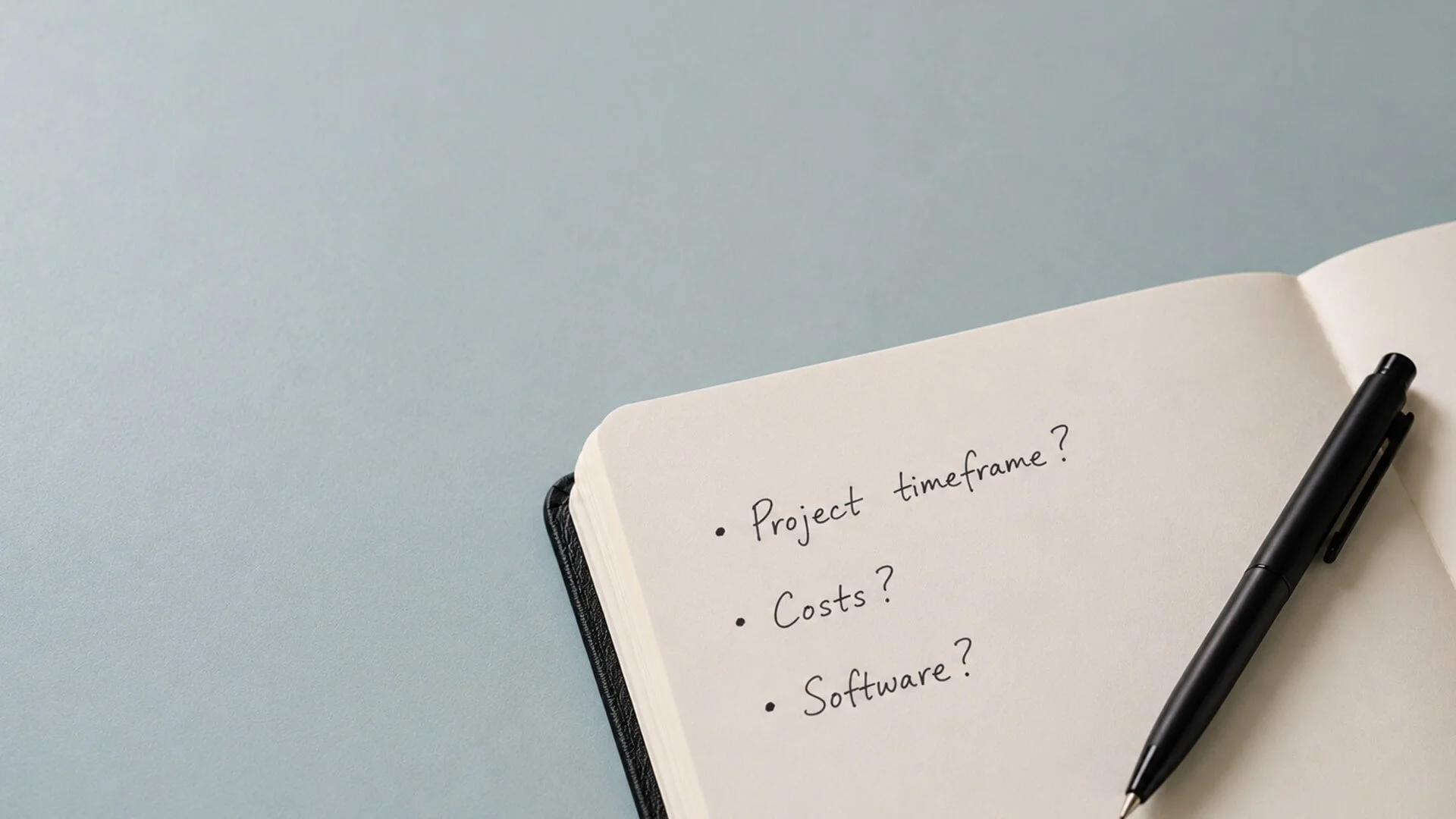 Open notebook with handwritten questions about project planning, including project timeframe, costs, and software, with black pen resting on the page, against a light blue background.