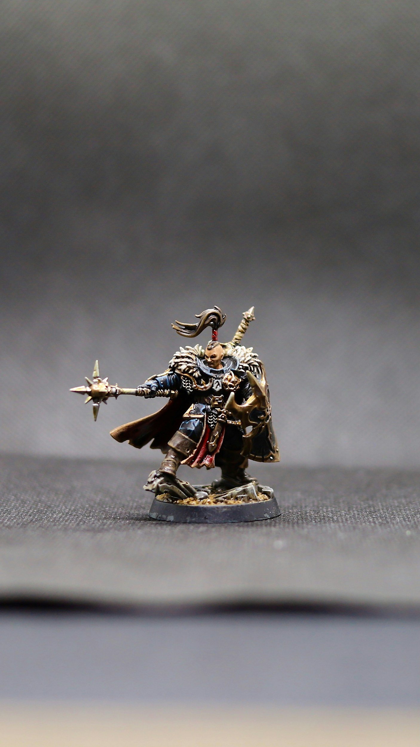 A miniature painted figurine of a fantasy warrior with a dark outfit, holding a staff in one hand and a shield in the other, standing on a round base.