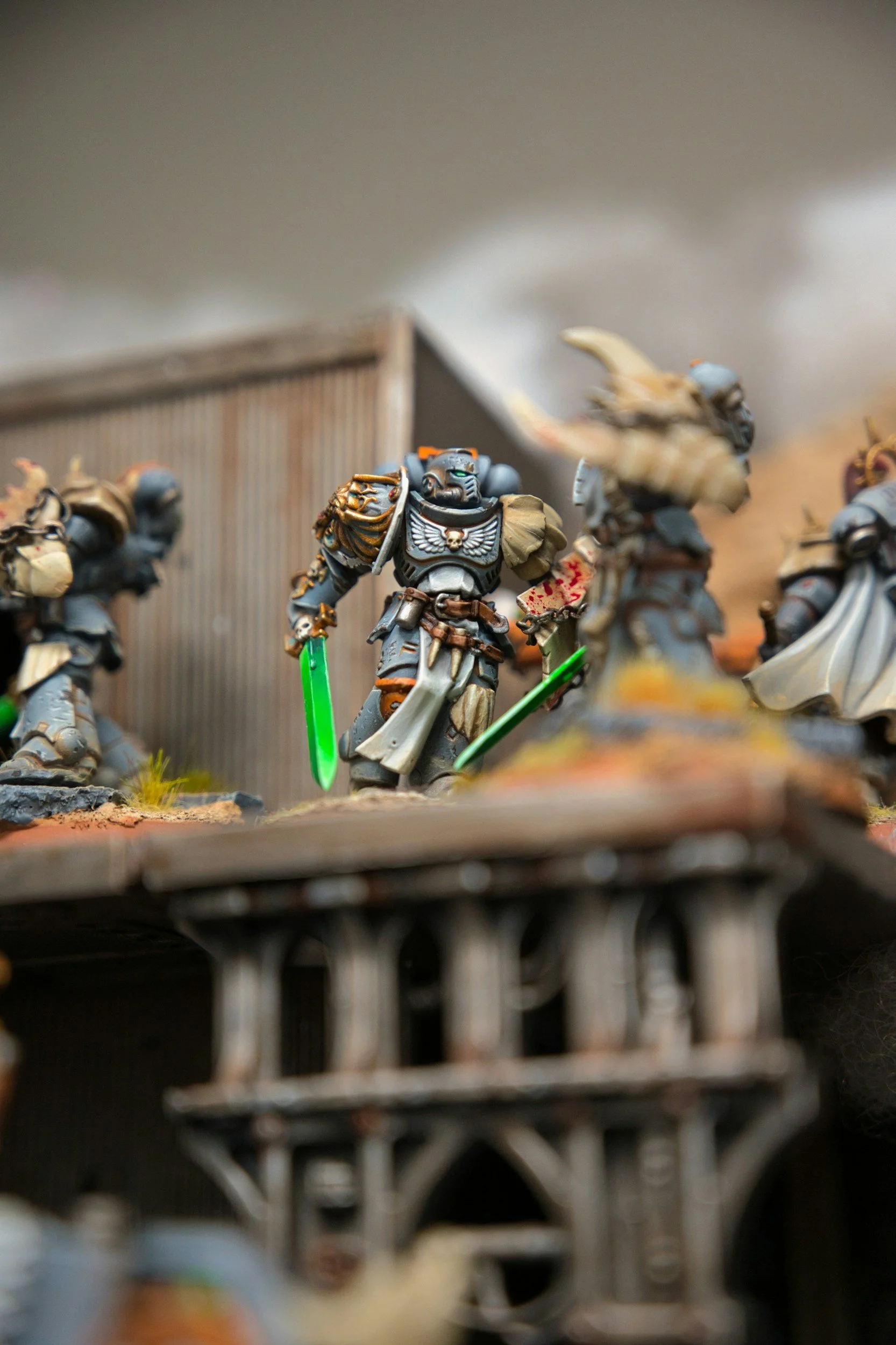 Close-up of painted miniature figures of space marines with glowing green swords, positioned on a detailed tabletop gaming terrain with a blurred background.