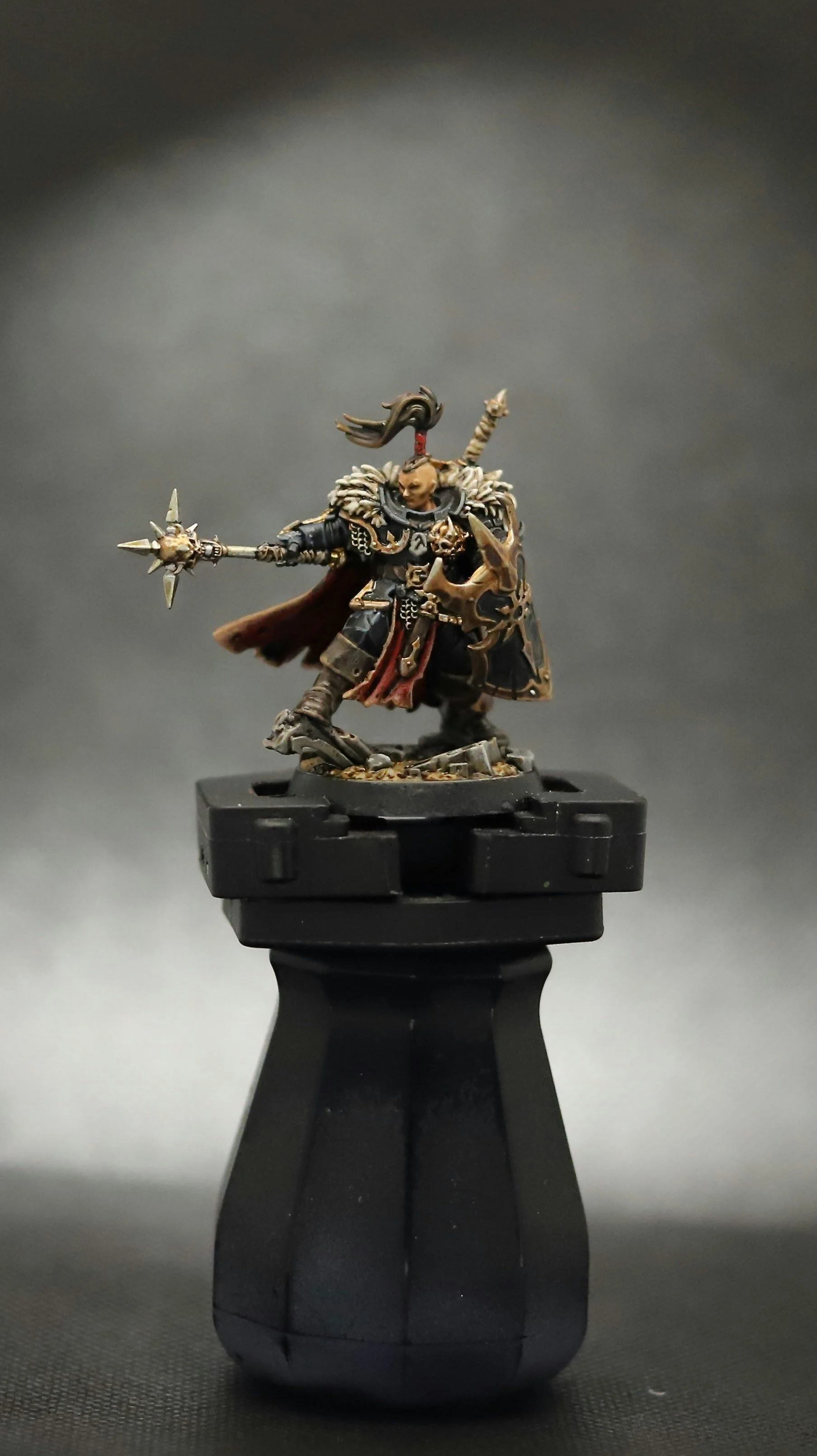 Miniature figurine of a fantasy warrior with armor, weapon, and shield, standing on a black base.