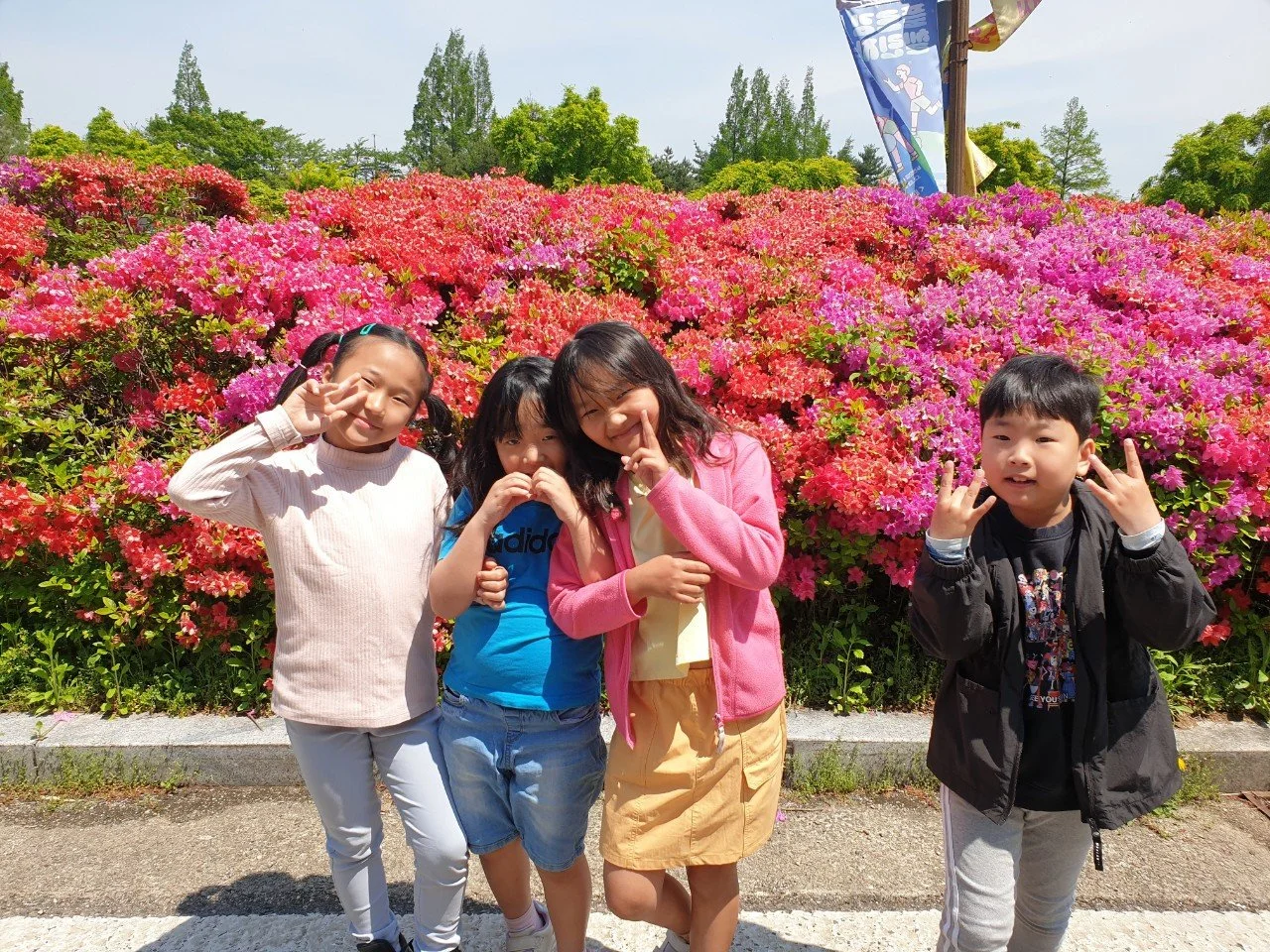 꽃밭 앞에서 포즈를 취하는 네 명의 어린이들, 봄날 화창한 날씨와 함께 즐거운 모습.