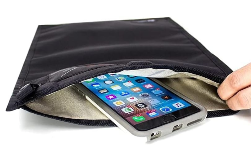 A hand opening a black padded sleeve with a smartphone inside, resting on a white surface.