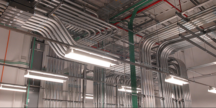Ceiling with multiple metal pipes and fluorescent lights in an industrial or commercial building.