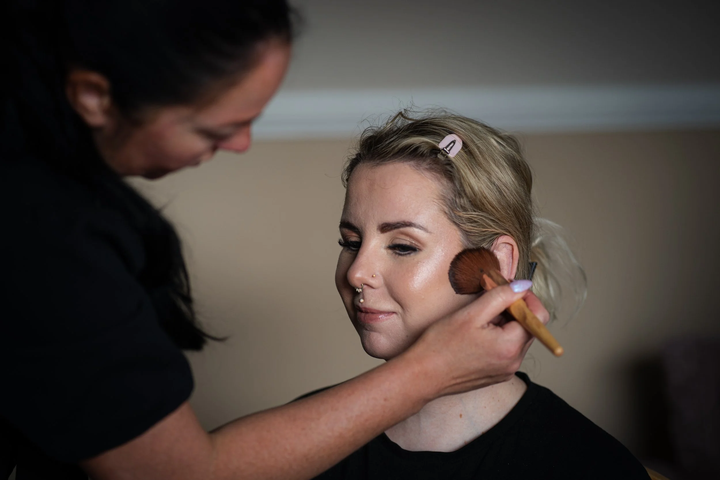Makeup artist applying blush to a woman's cheeks with a brush.