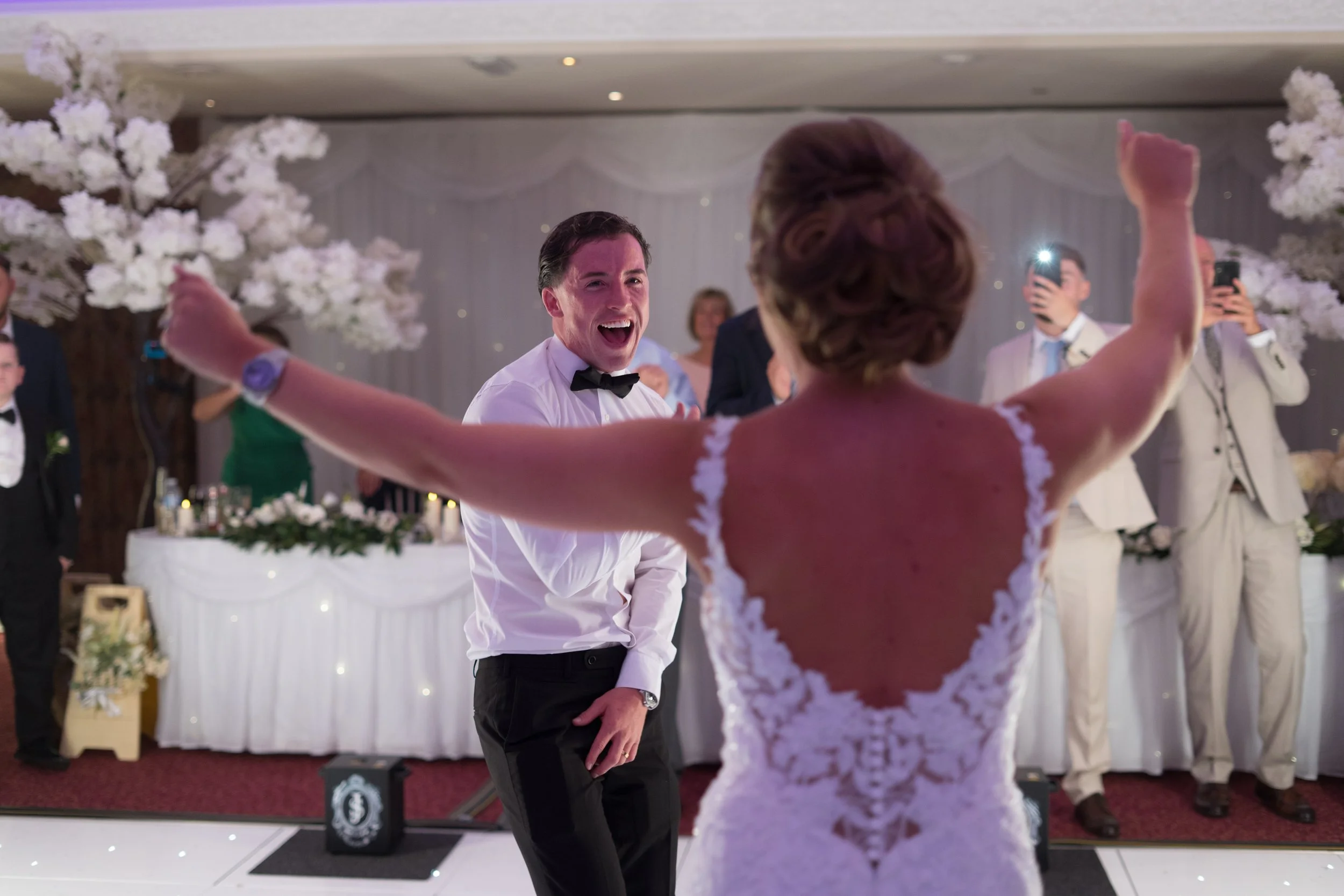 A bride and groom dancing and celebrating at their wedding reception, with the bride facing away and the groom smiling and looking happy.