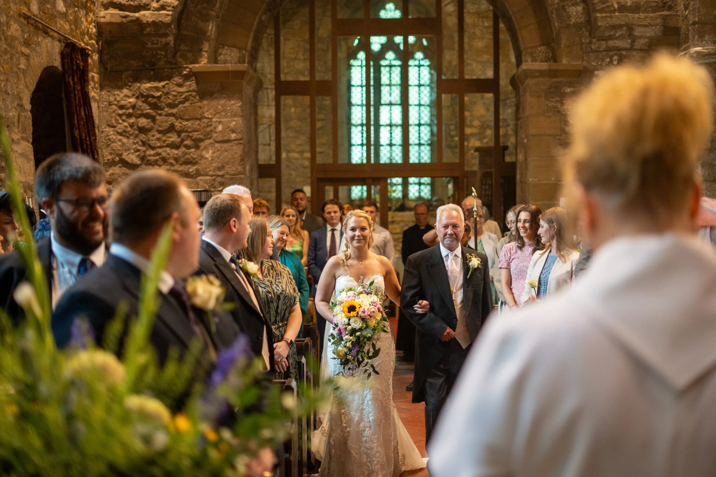 A bride walking down the aisle with her father in a church filled with wedding guests.
