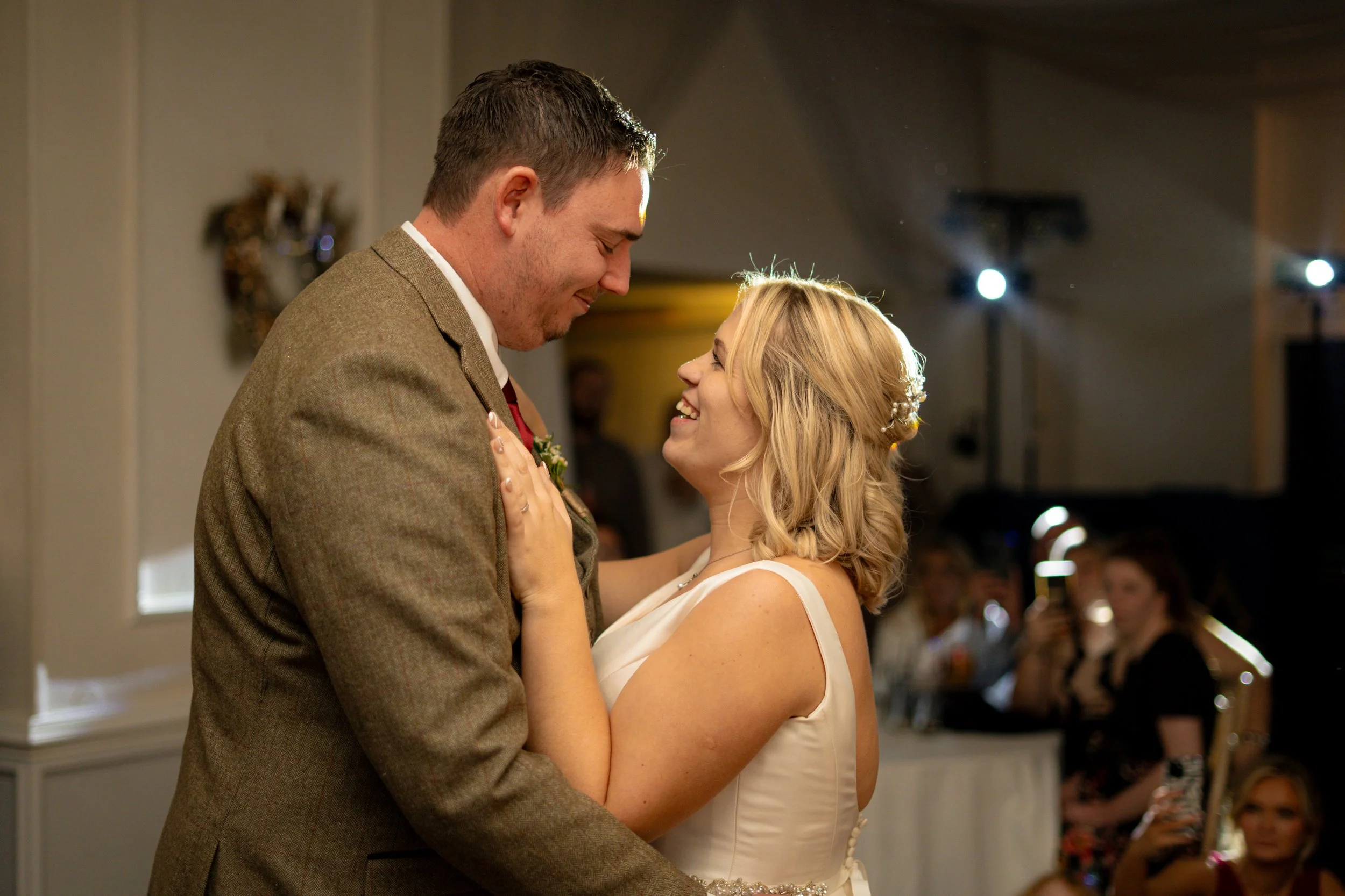 A newlywed couple sharing a dance at their wedding reception, gazing into each other's eyes and smiling.