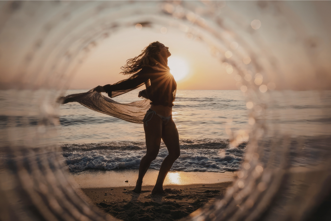 Femme sur la plage au coucher du soleil vue à travers un cercle en verre. Expansion d'âme et d'abondance.