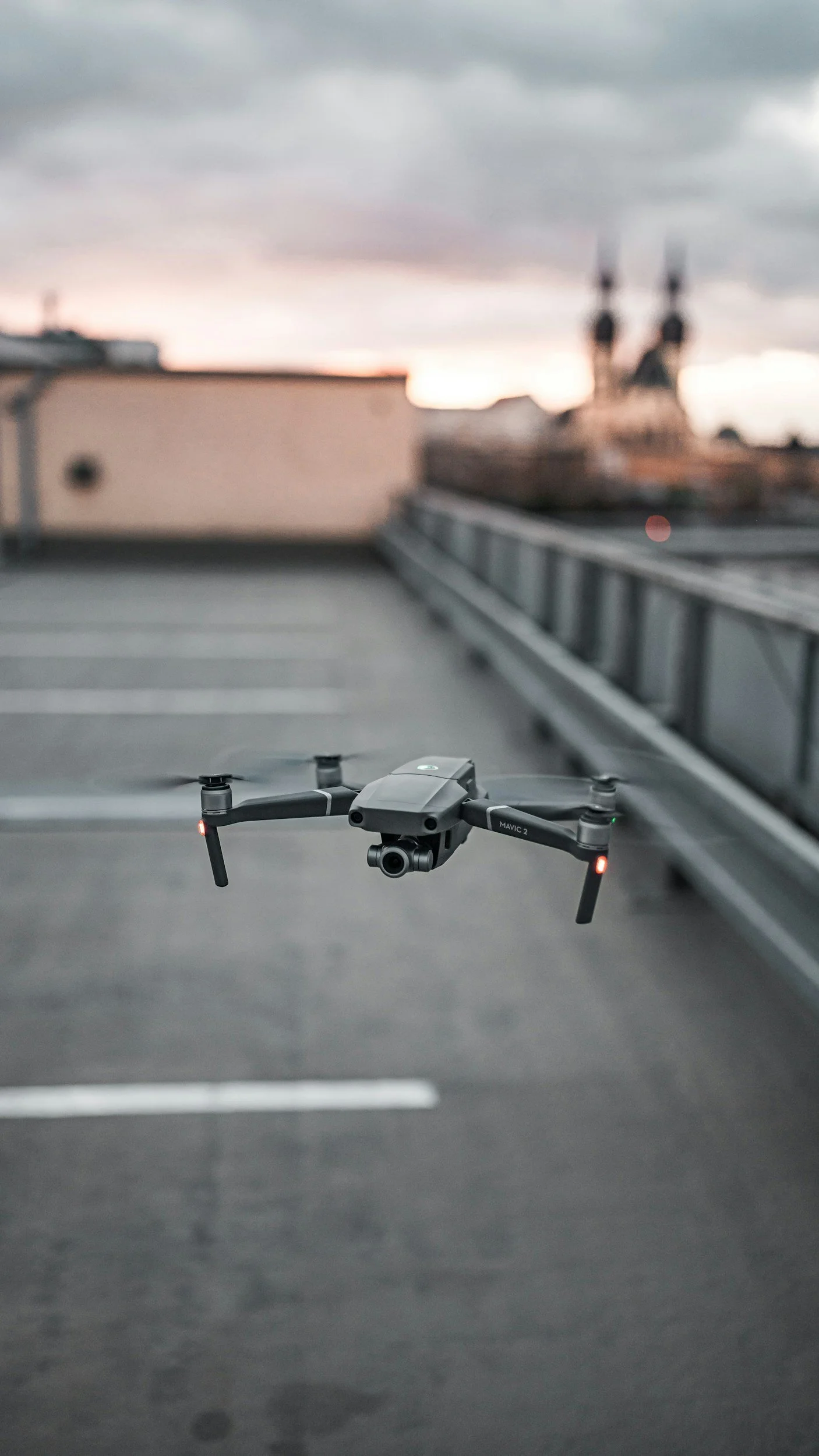 A drone flying in a parking lot at sunset with buildings and a church steeple in the background.