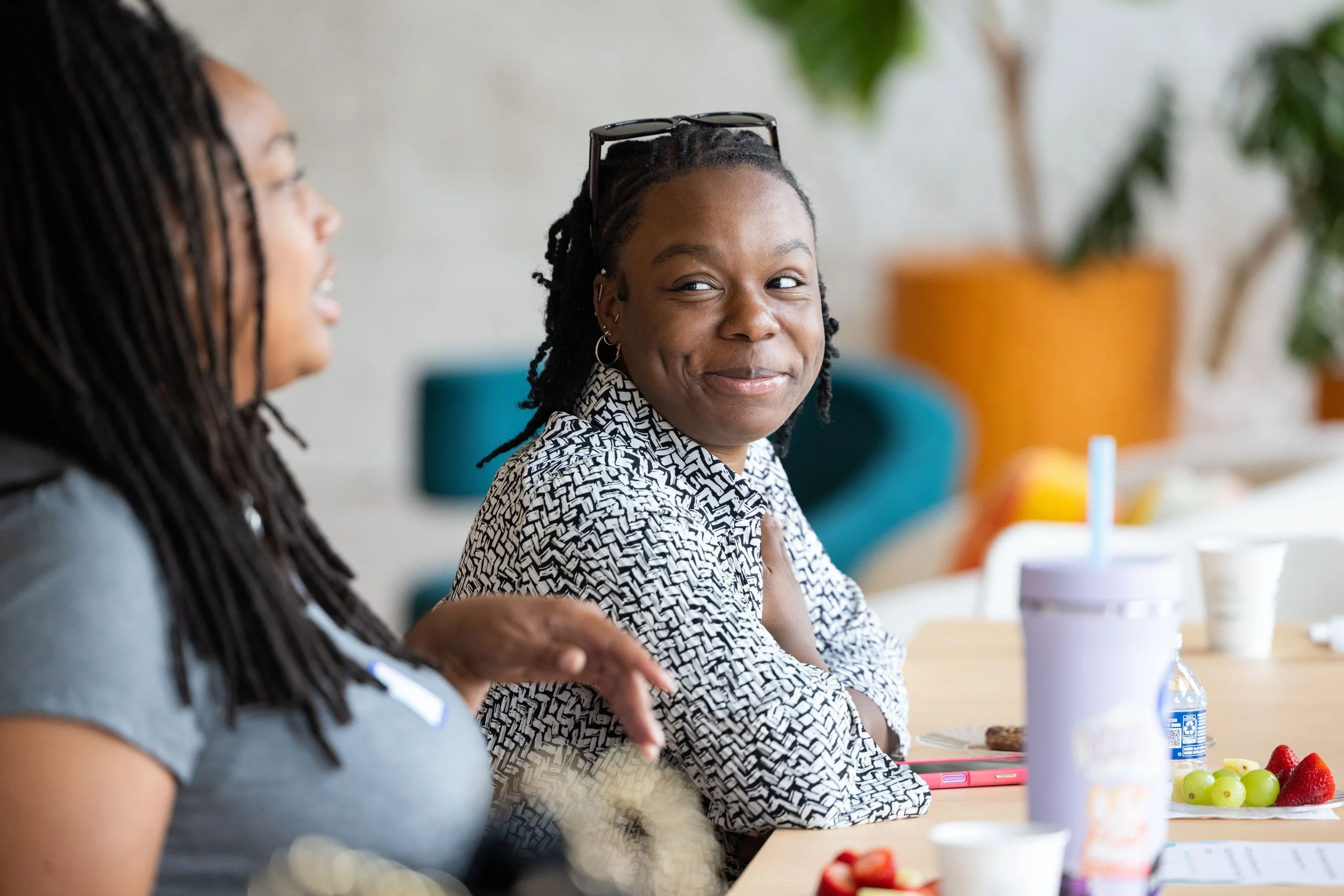 Two women sitting at a table having a conversation, with food and drinks on the table.