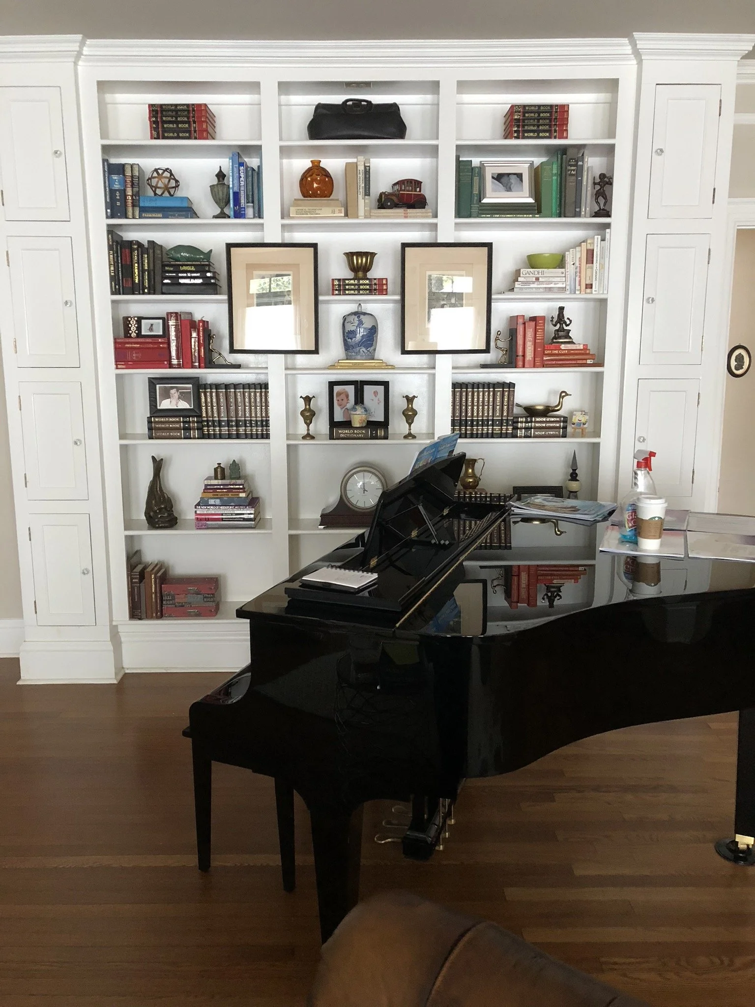 Interior of a room with a grand piano, a large white bookshelf filled with books and decorative items.
