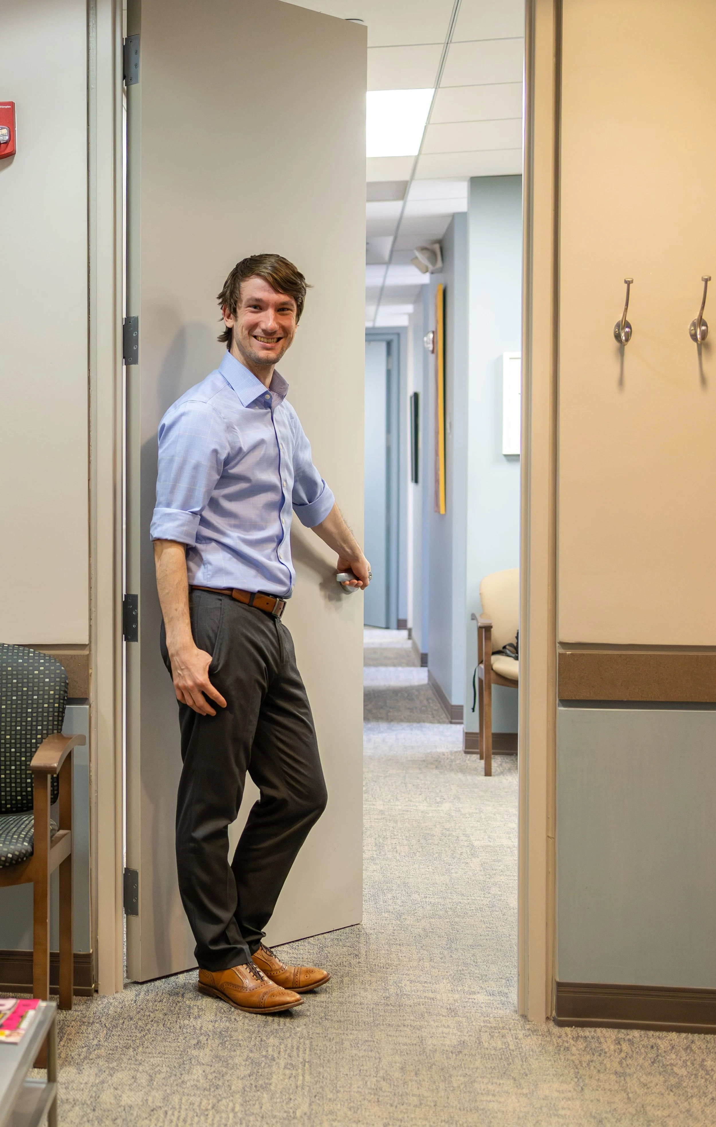 Dr. Brian Havel, a dentist in a blue shirt and grey pants, stands smiling and welcoming you in to the open door of his office