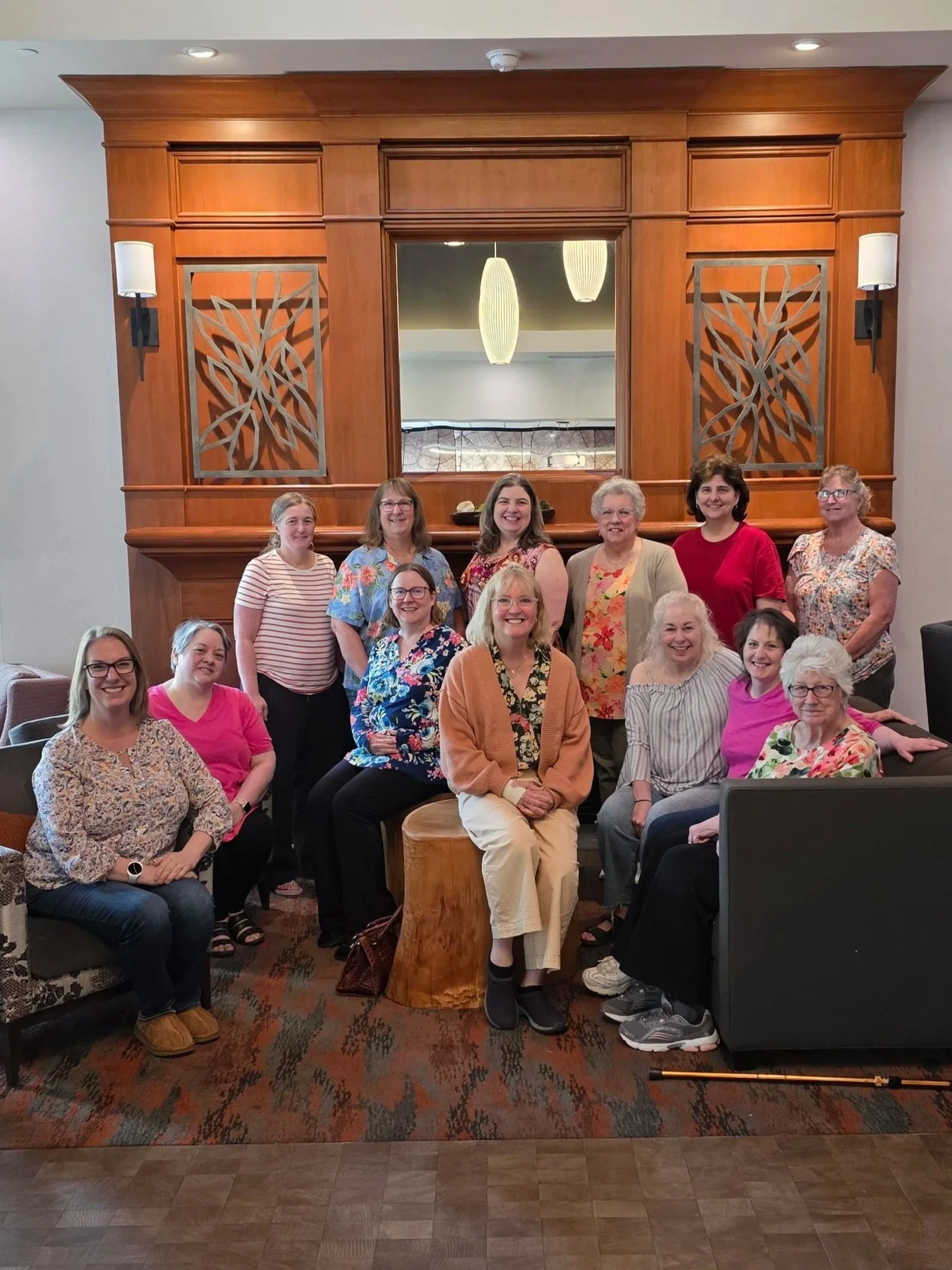 Group of women posing for a photo in a room with wood paneling and a large mirror behind them.