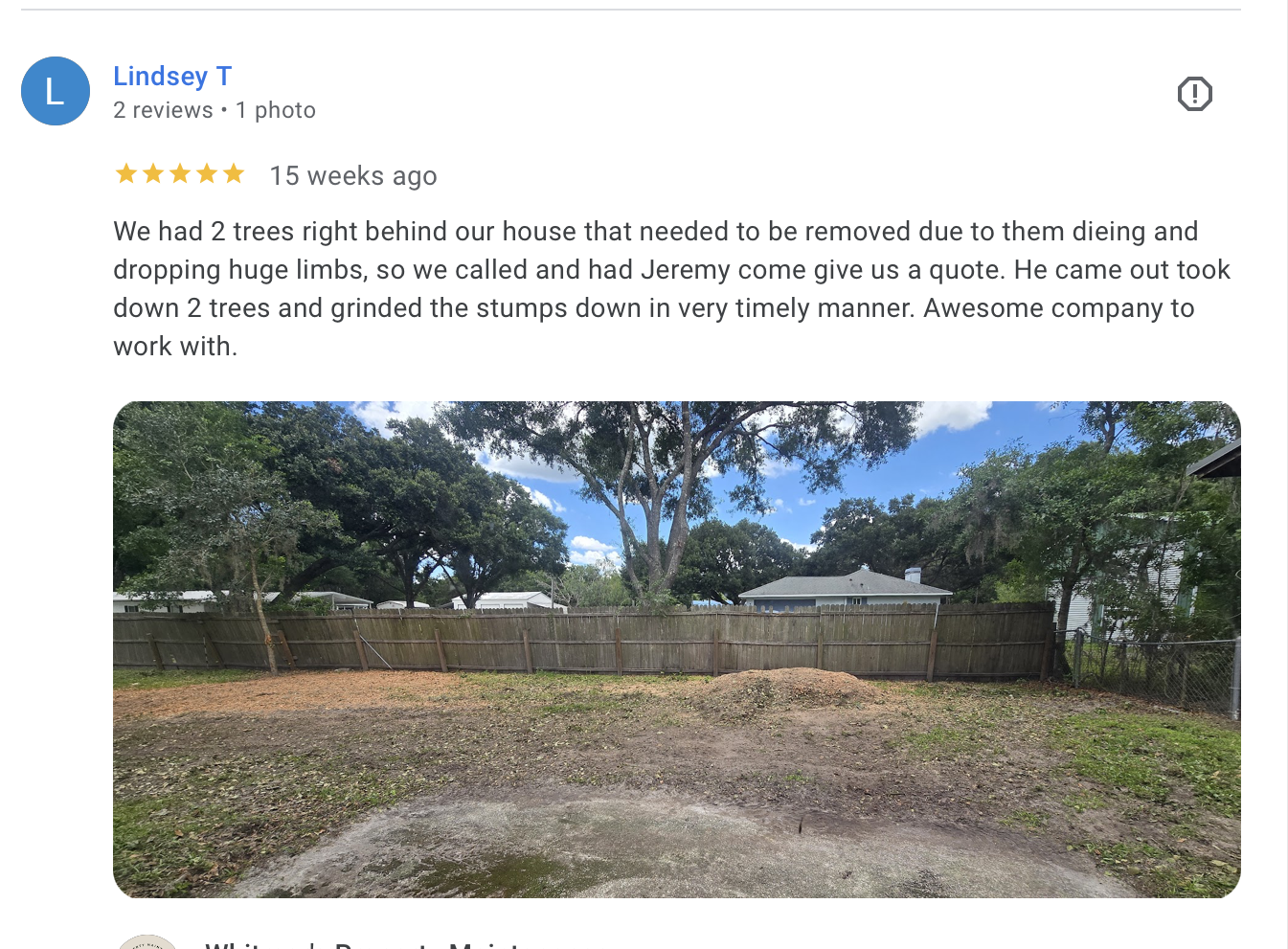 Backyard with dirt patch, trees, wooden fence, and neighboring houses under a partly cloudy sky.