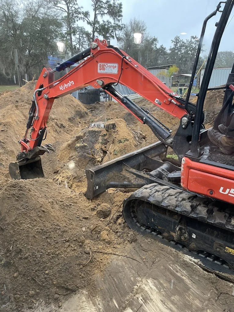 A red Kubota mini excavator digging into dirt at a construction site.
