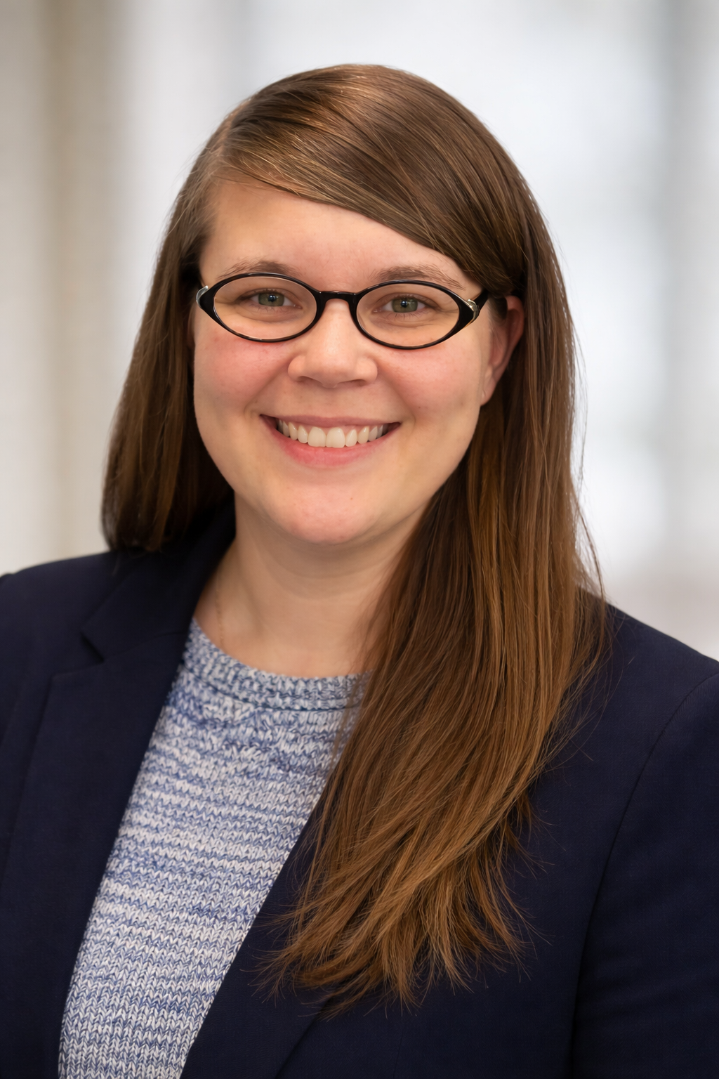 A smiling woman with long brown hair, glasses, and a blazer.